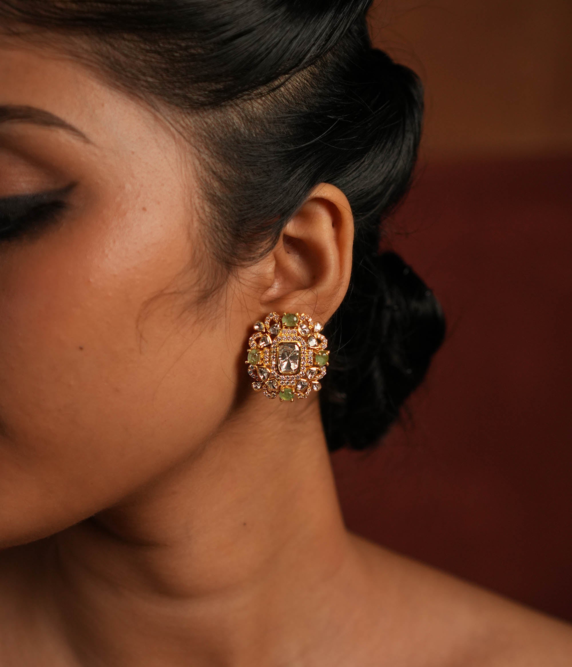 A beautifully crafted gold-plated silver stud earring featuring a dazzling Polki stone at the center, elegantly surrounded by a layer of shimmering CZ stones and vibrant green cut stones. This exquisite design adds a touch of sophistication, making it a perfect accessory for both traditional and contemporary looks.