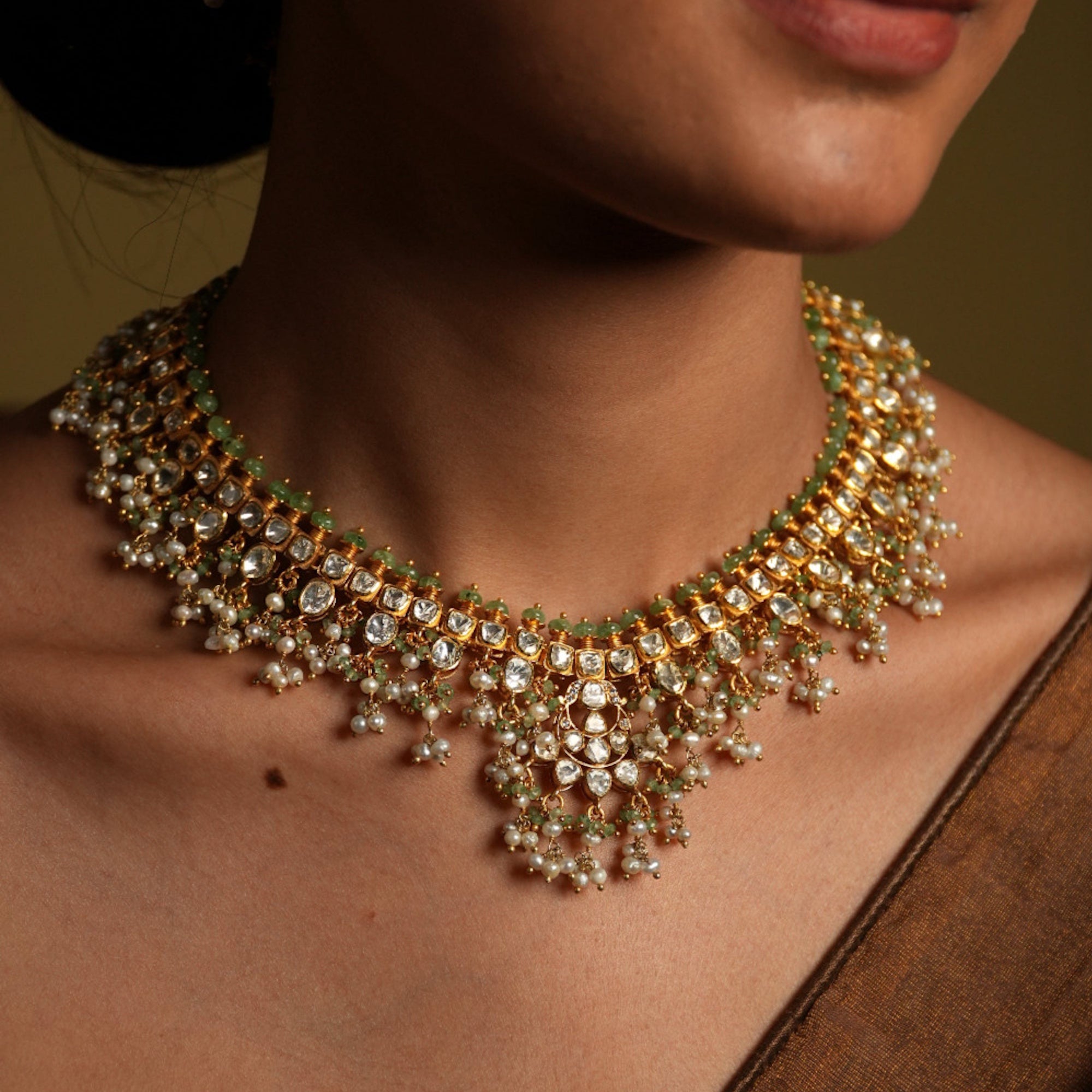 Close-up of a person wearing an ornate necklace with green and gold accents.