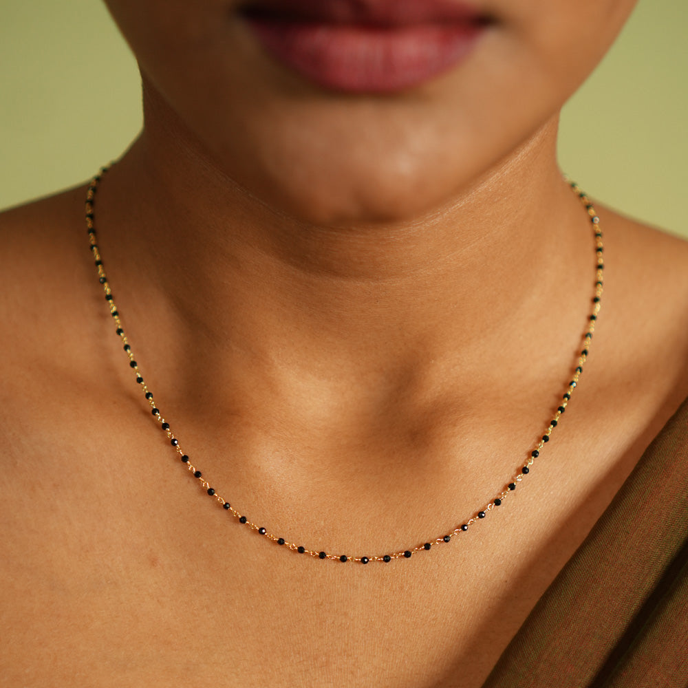 Woman wearing a delicate silver Mangal Sutra chain with gold plating, featuring black beads and subtle gold accents, resting gracefully on her neckline, paired with a muted saree in earthy tones.