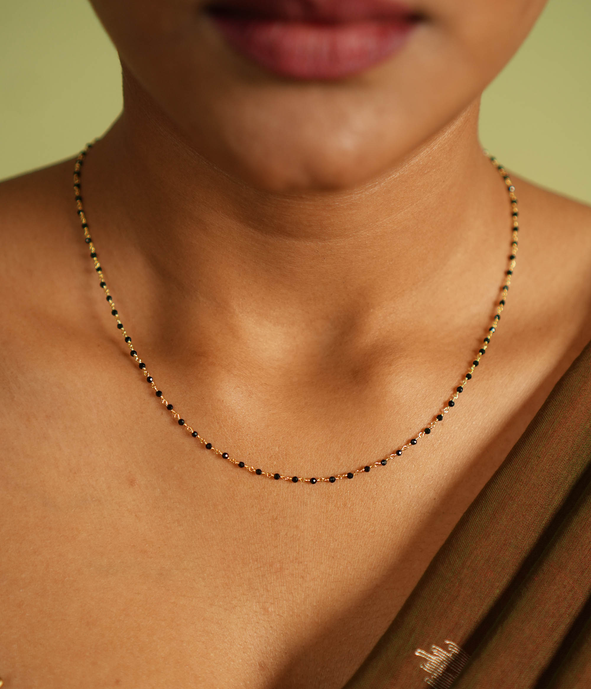 Woman wearing a delicate silver Mangal Sutra chain with gold plating, featuring black beads and subtle gold accents, resting gracefully on her neckline, paired with a muted saree in earthy tones.