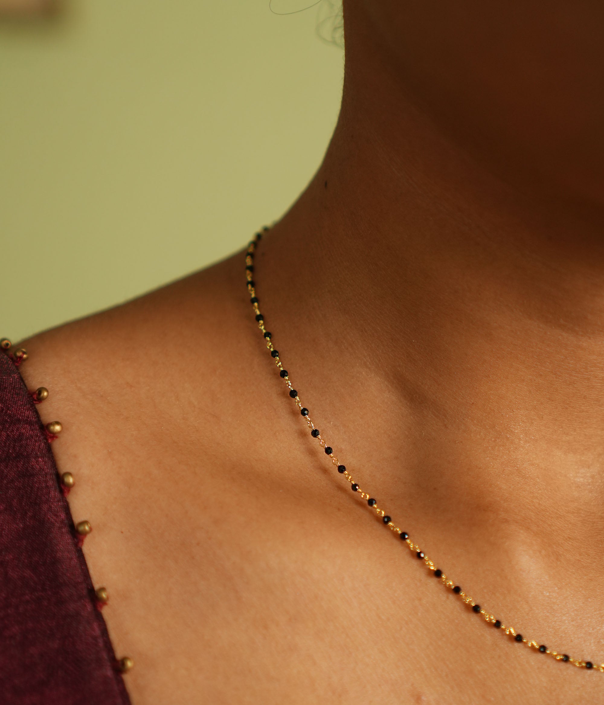 Woman wearing a delicate silver Mangal Sutra chain with gold plating, featuring black beads and subtle gold accents, resting gracefully on her neckline, paired with a muted saree in earthy tones.