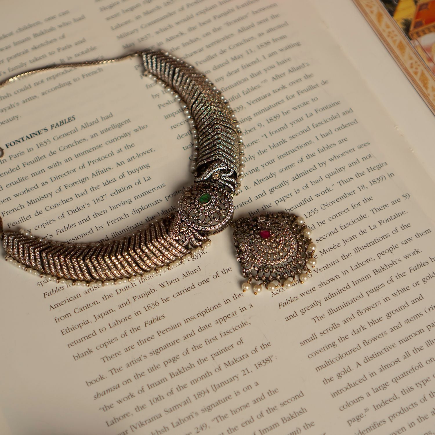 This gold-plated silver necklace features a captivating blend of gemstones. It showcases a central emerald pendant, flanked by rubies and smaller clear stones, likely cubic zirconia. The necklace is further embellished with accents of freshwater pearls, creating a luxurious and elegant look.