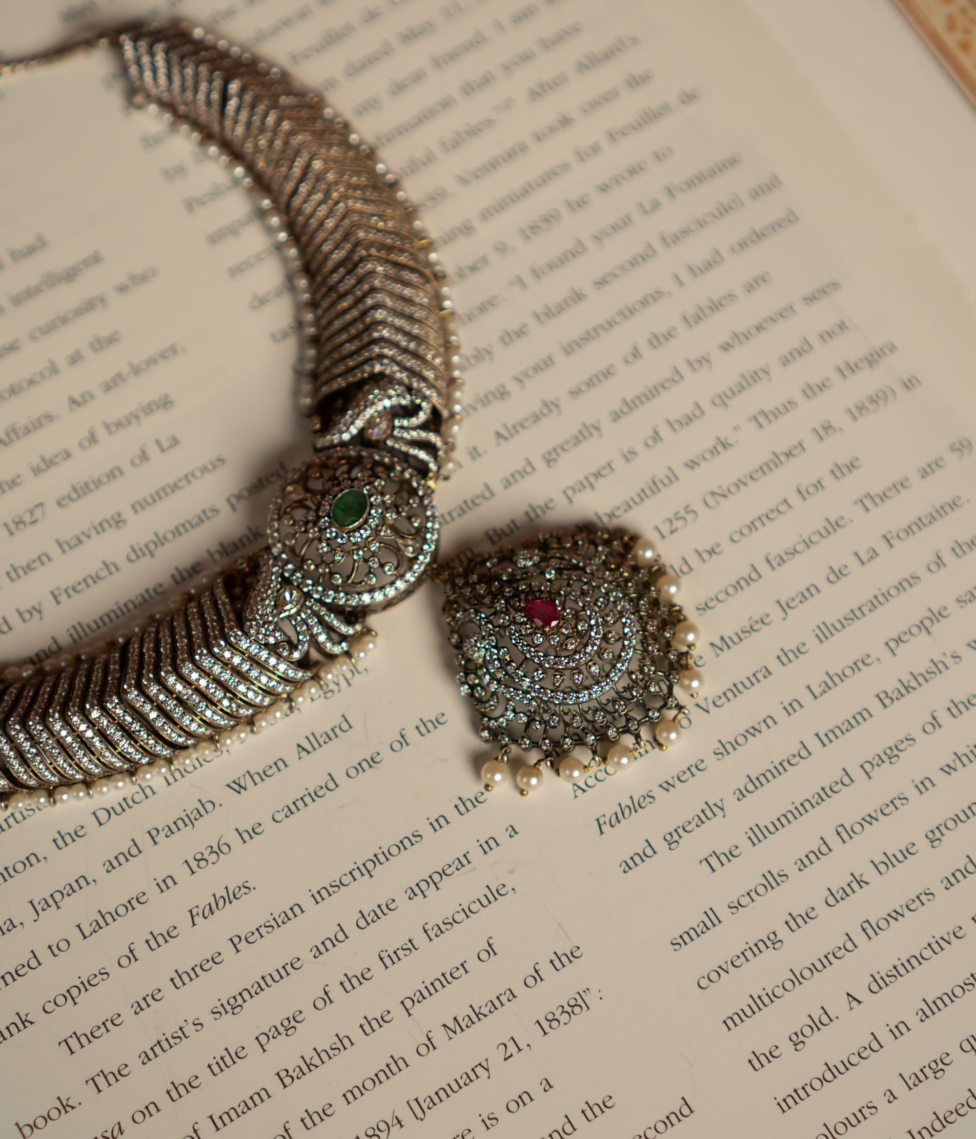 This gold-plated silver necklace features a captivating blend of gemstones. It showcases a central emerald pendant, flanked by rubies and smaller clear stones, likely cubic zirconia. The necklace is further embellished with accents of freshwater pearls, creating a luxurious and elegant look.