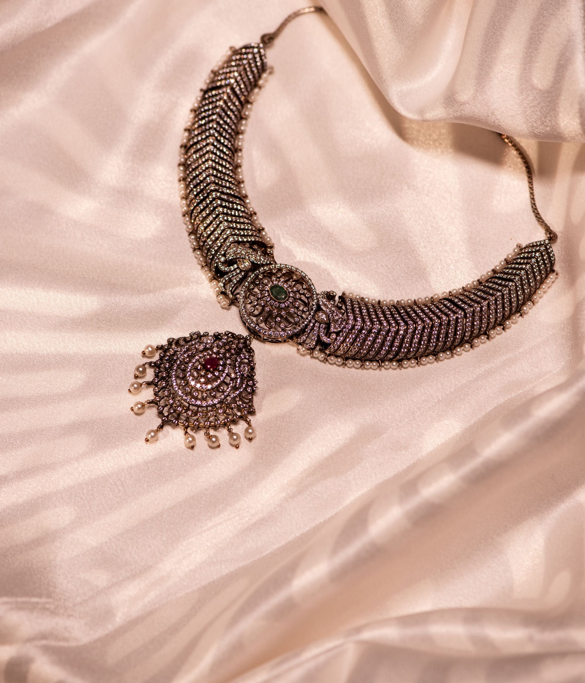 This gold-plated silver necklace features a captivating blend of gemstones. It showcases a central emerald pendant, flanked by rubies and smaller clear stones, likely cubic zirconia. The necklace is further embellished with accents of freshwater pearls, creating a luxurious and elegant look.