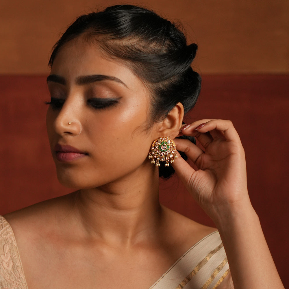 A beautifully crafted gold-plated silver drop earring featuring a dazzling Polki stone at the center, elegantly surrounded by a layer of shimmering CZ stones and vibrant green cut stones. The design is completed with delicate white pearl drops, adding a touch of grace and sophistication, making it a perfect accessory for both traditional and contemporary looks.