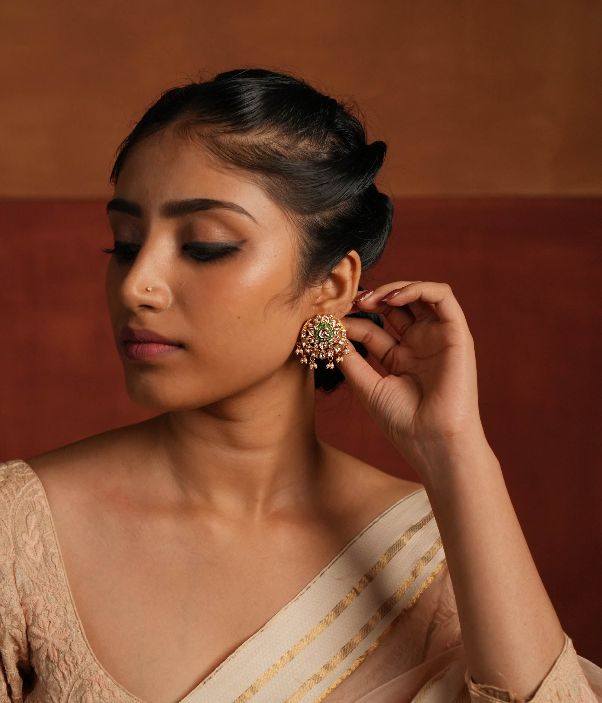 A beautifully crafted gold-plated silver drop earring featuring a dazzling Polki stone at the center, elegantly surrounded by a layer of shimmering CZ stones and vibrant green cut stones. The design is completed with delicate white pearl drops, adding a touch of grace and sophistication, making it a perfect accessory for both traditional and contemporary looks.