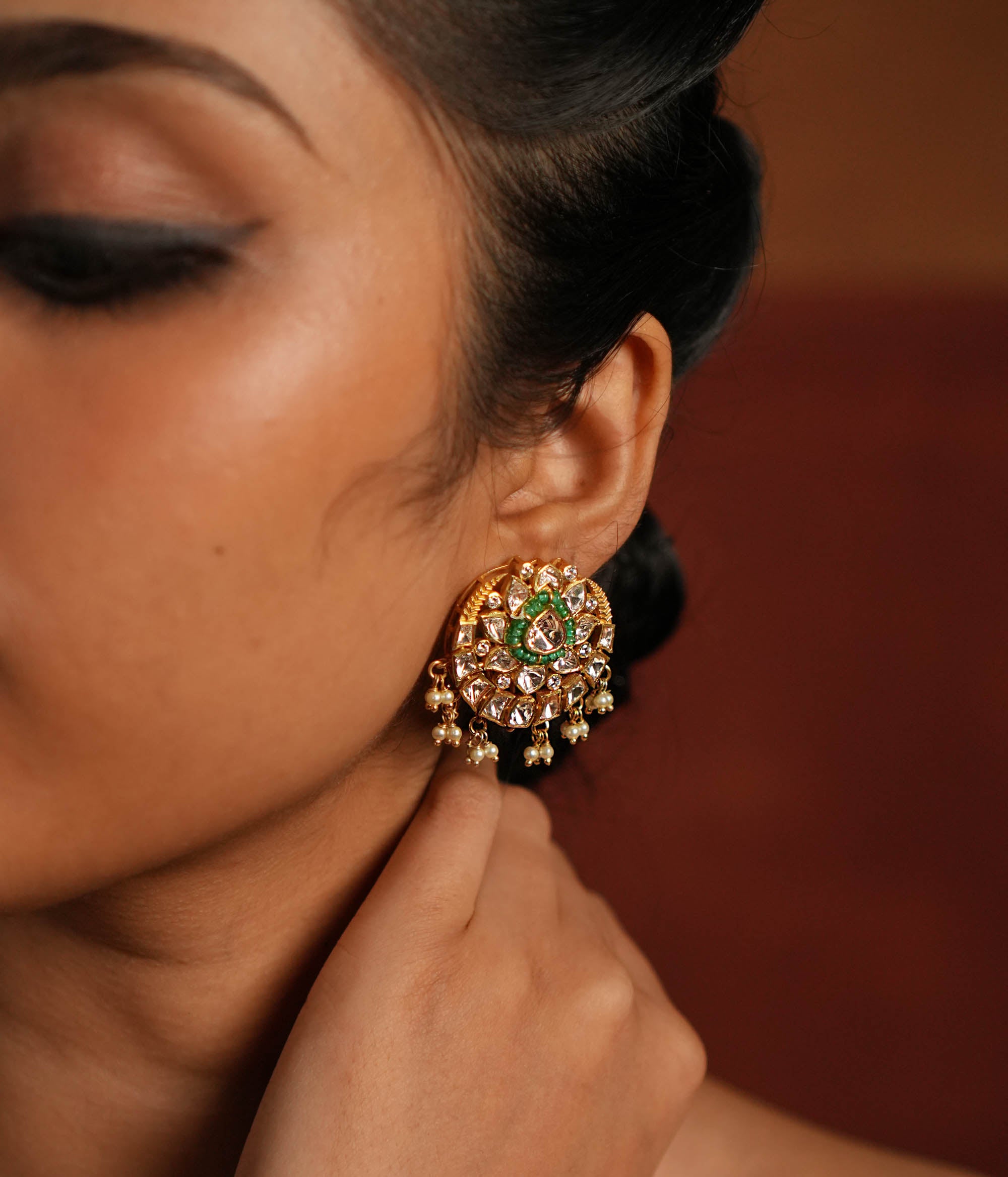 A beautifully crafted gold-plated silver drop earring featuring a dazzling Polki stone at the center, elegantly surrounded by a layer of shimmering CZ stones and vibrant green cut stones. The design is completed with delicate white pearl drops, adding a touch of grace and sophistication, making it a perfect accessory for both traditional and contemporary looks.