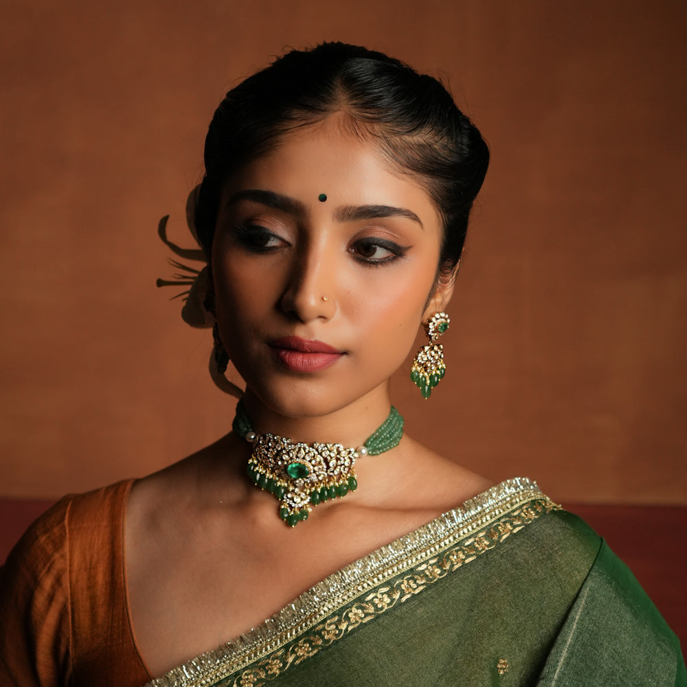 Victorian elegance reborn! This gold-plated silver choker features a striking green gemstone at its heart, surrounded by dazzling polki and CZ stones. Delicate pearl drops with golden beads enhance its timeless allure, whispering tales of a bygone era. A perfect blend of heritage and grace for the modern woman.