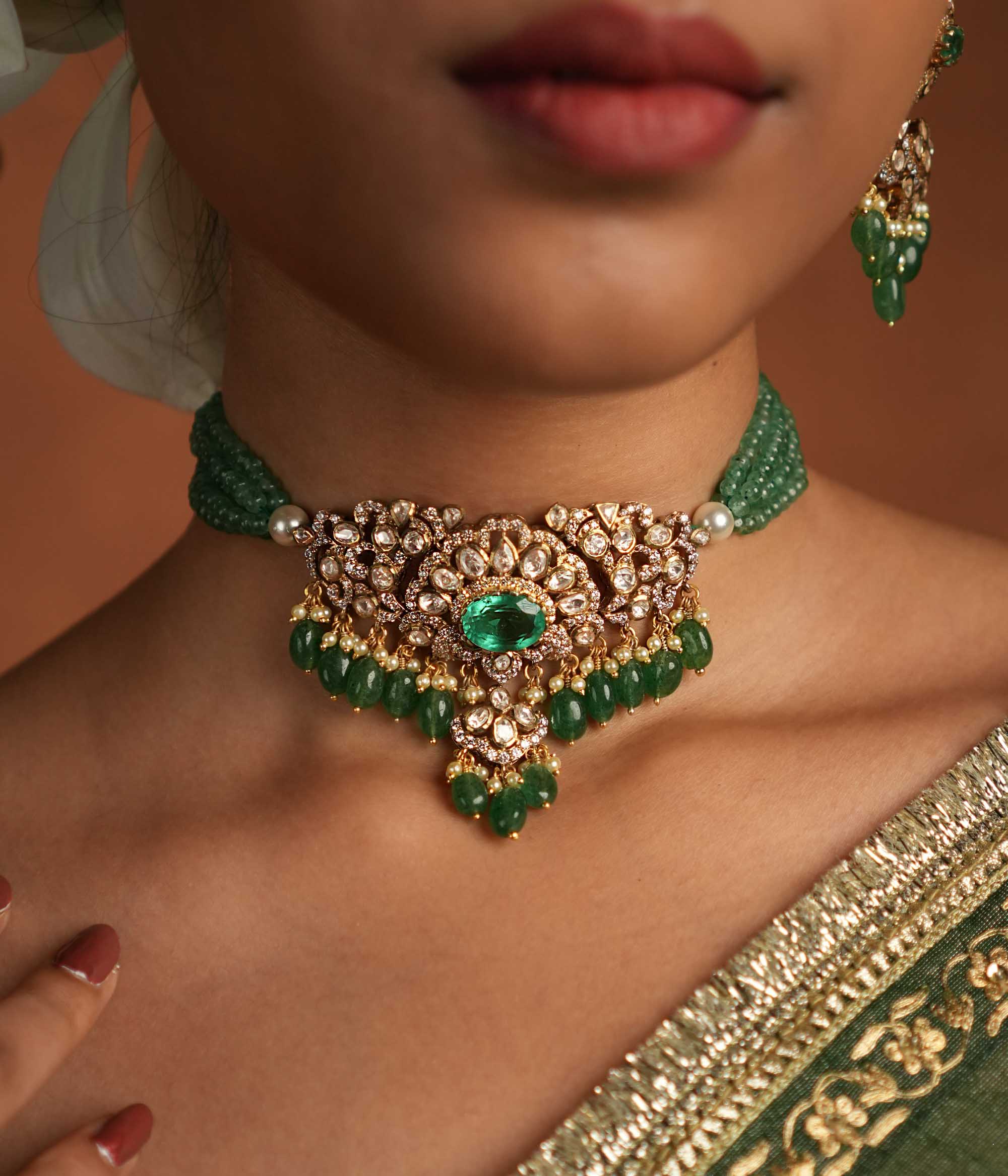 Victorian elegance reborn! This gold-plated silver choker features a striking green gemstone at its heart, surrounded by dazzling polki and CZ stones. Delicate pearl drops with golden beads enhance its timeless allure, whispering tales of a bygone era. A perfect blend of heritage and grace for the modern woman.