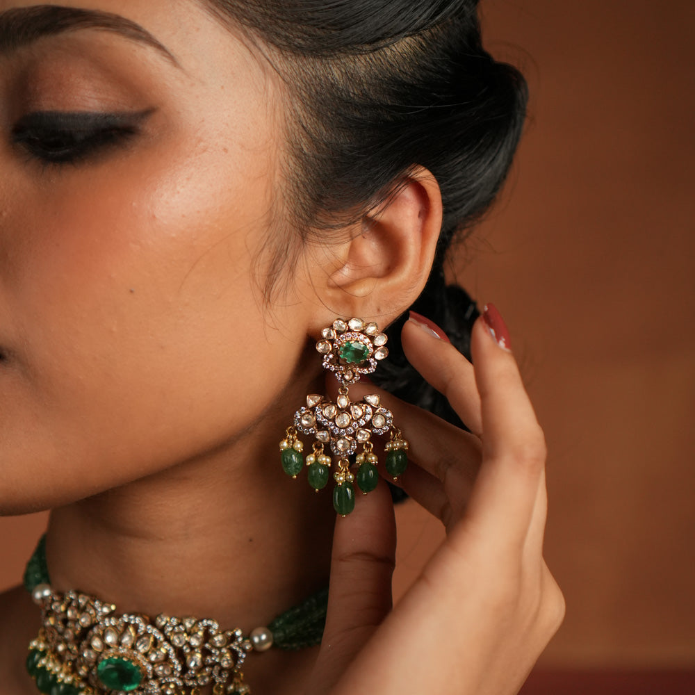 Victorian elegance reborn! These gold-plated silver dangler earrings feature a radiant green gemstone at the center, encircled by shimmering polki and CZ stones. Graceful pearl drops with golden beads enhance their charm, evoking the allure of a forgotten era. A timeless statement of beauty, crafted for the modern woman.