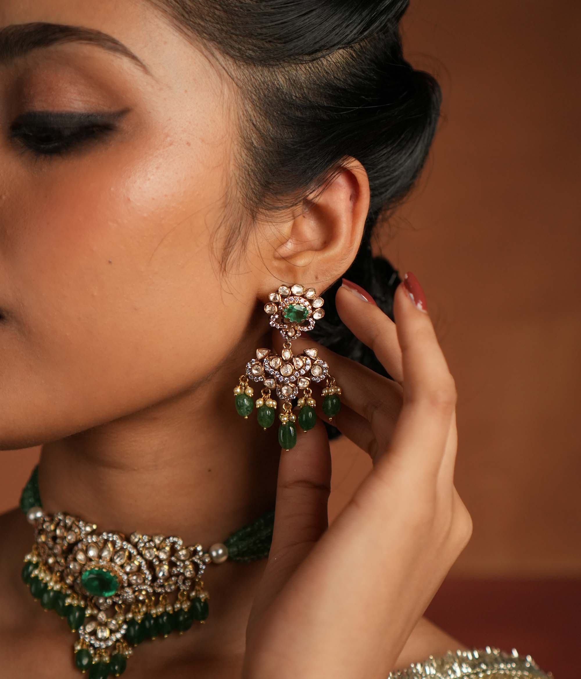 Victorian elegance reborn! These gold-plated silver dangler earrings feature a radiant green gemstone at the center, encircled by shimmering polki and CZ stones. Graceful pearl drops with golden beads enhance their charm, evoking the allure of a forgotten era. A timeless statement of beauty, crafted for the modern woman.