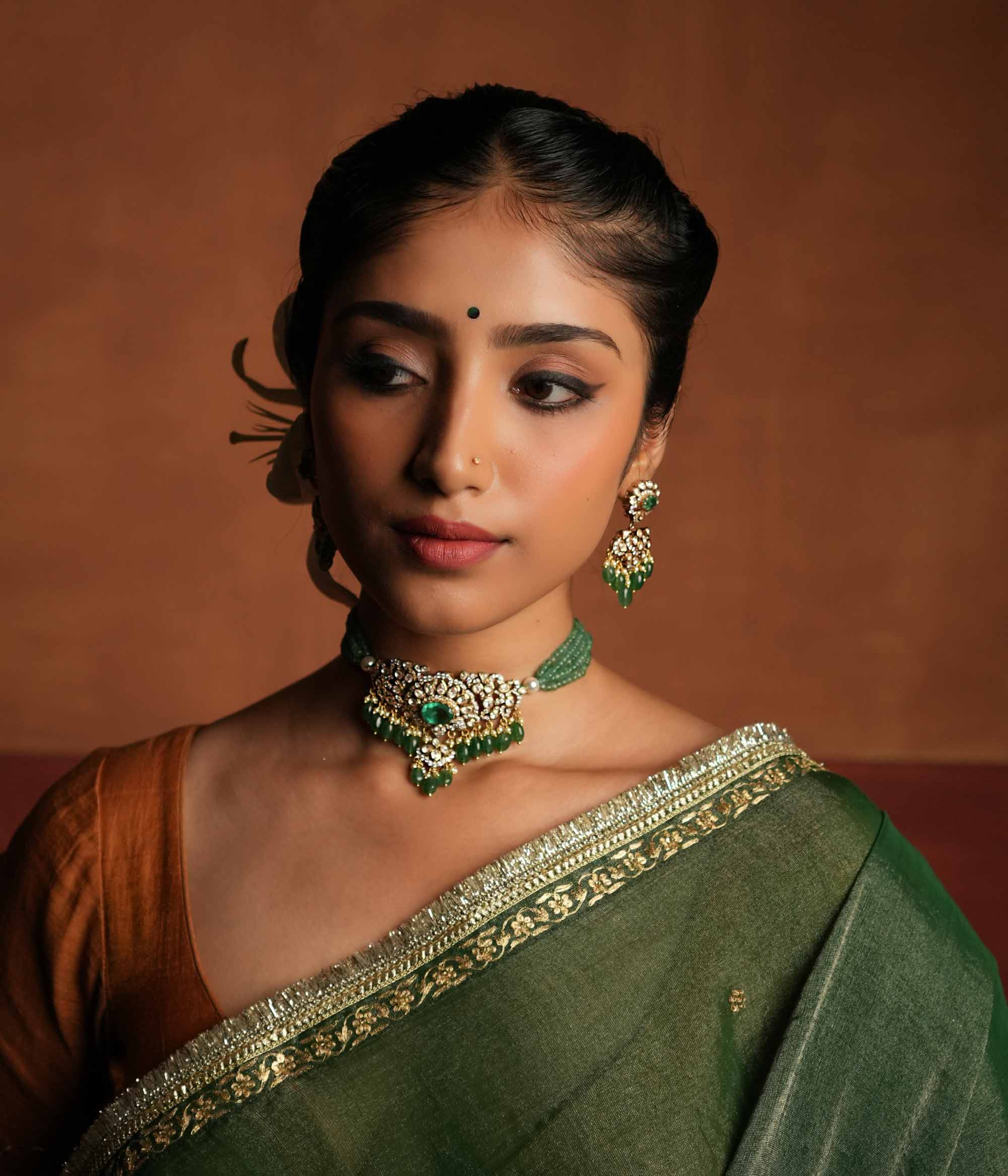 Victorian elegance reborn! These gold-plated silver dangler earrings feature a radiant green gemstone at the center, encircled by shimmering polki and CZ stones. Graceful pearl drops with golden beads enhance their charm, evoking the allure of a forgotten era. A timeless statement of beauty, crafted for the modern woman.
