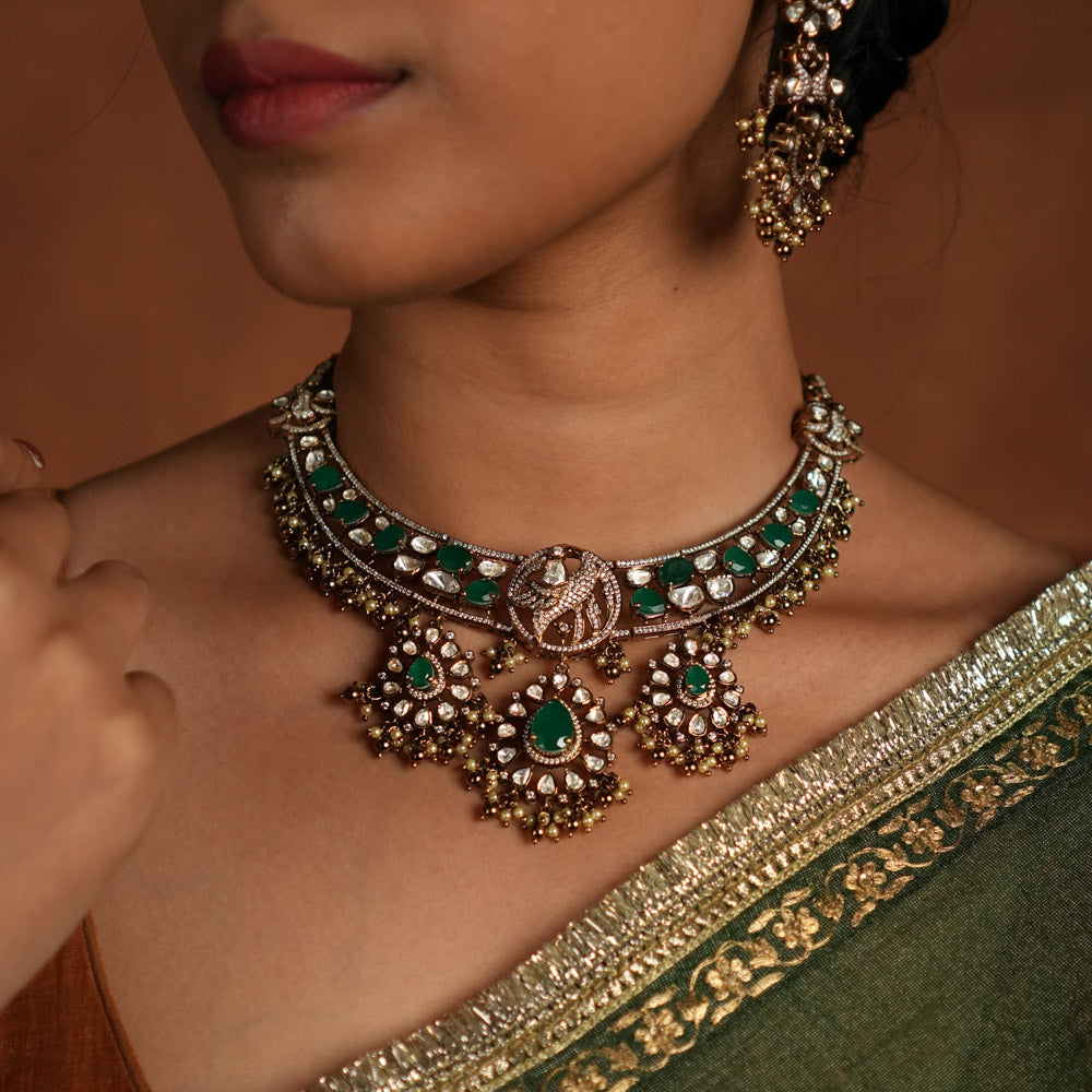 Victorian opulence reborn! This gold-plated silver choker necklace features a dazzling combination of CZ stones, green gemstones, and polki stones. The chain is adorned with polki and green gemstones, while the pendant mirrors the same design, gracefully accented with delicate pearl drops. A timeless blend of heritage and luxury, redefined for modern elegance.