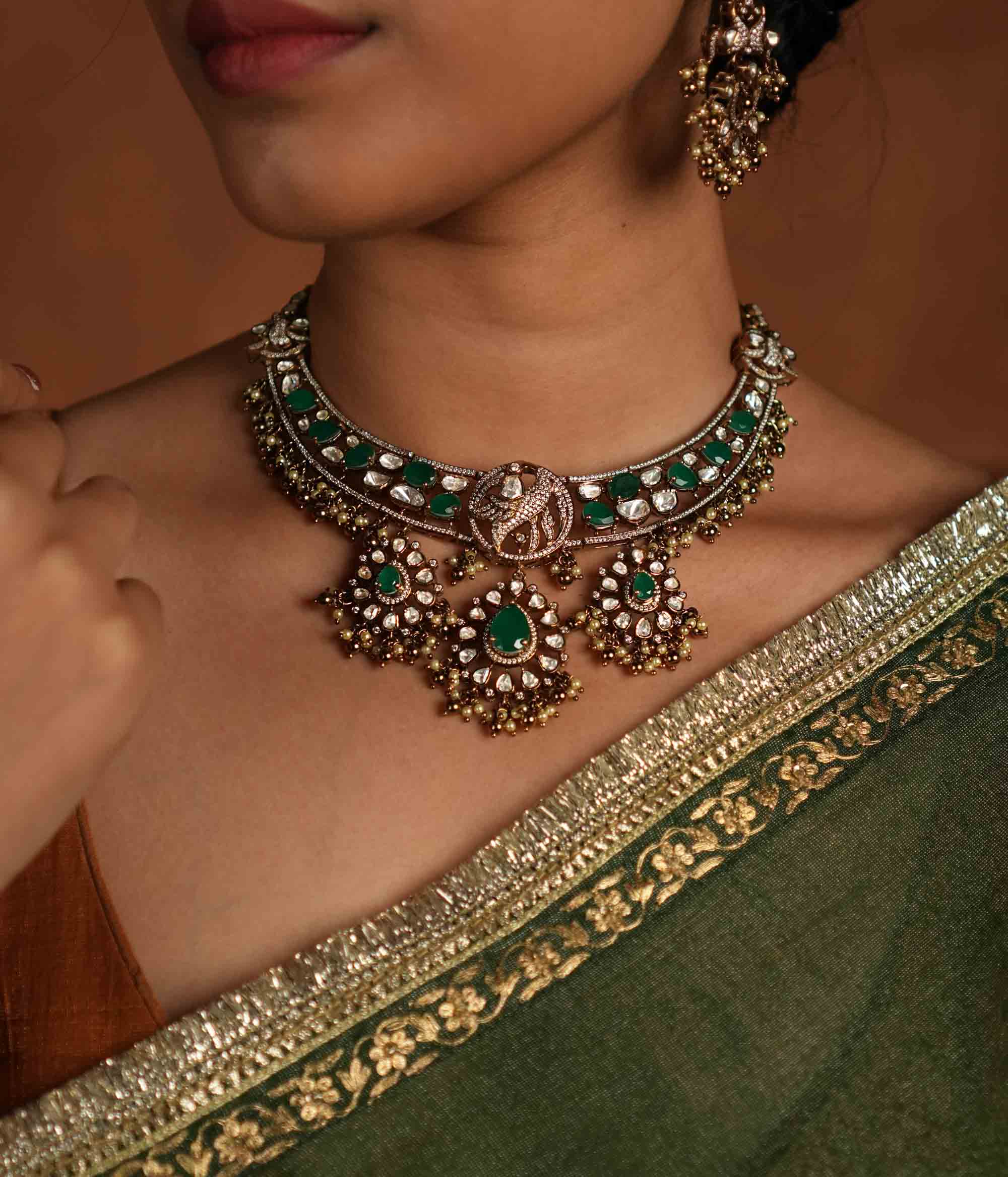 Victorian opulence reborn! This gold-plated silver choker necklace features a dazzling combination of CZ stones, green gemstones, and polki stones. The chain is adorned with polki and green gemstones, while the pendant mirrors the same design, gracefully accented with delicate pearl drops. A timeless blend of heritage and luxury, redefined for modern elegance.