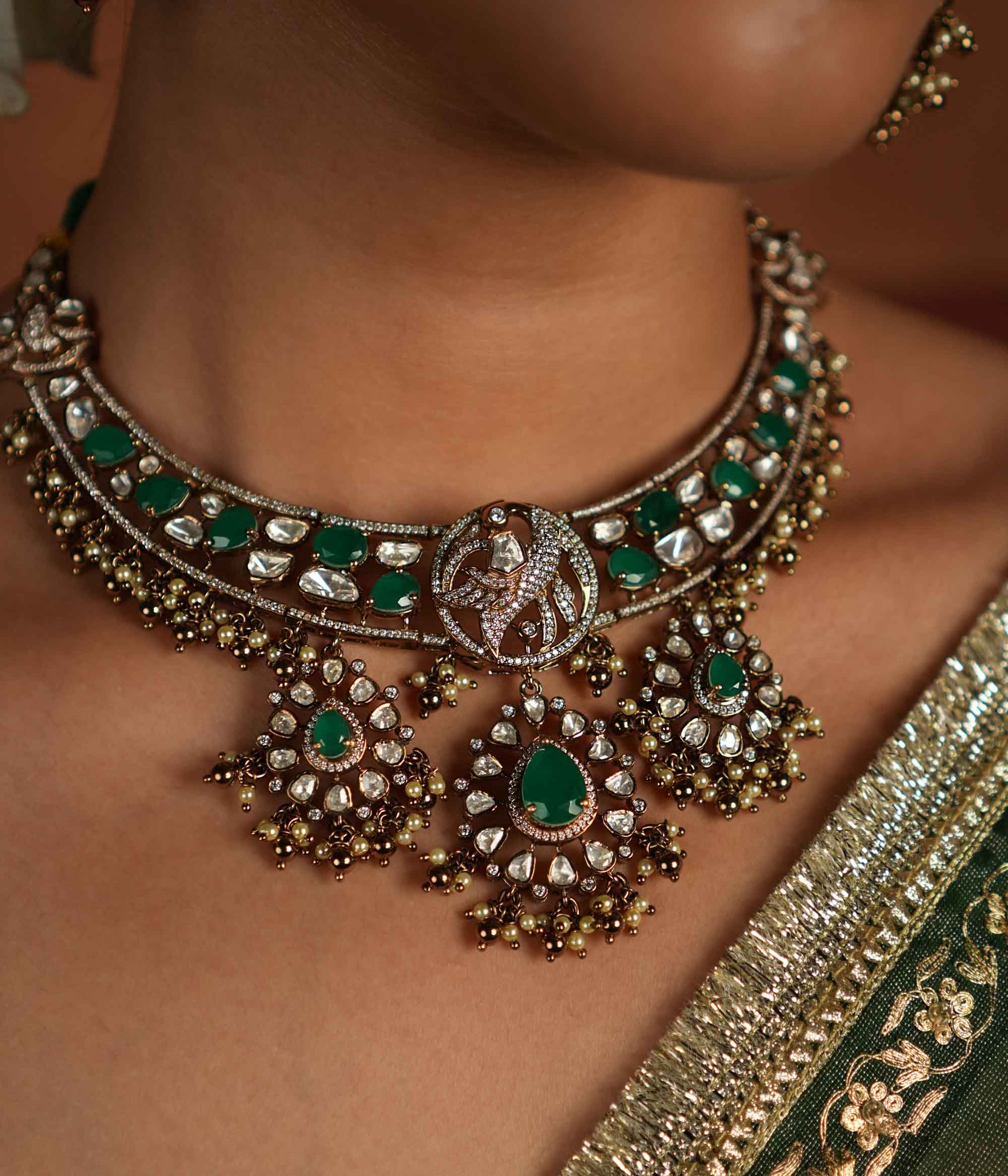 Victorian opulence reborn! This gold-plated silver choker necklace features a dazzling combination of CZ stones, green gemstones, and polki stones. The chain is adorned with polki and green gemstones, while the pendant mirrors the same design, gracefully accented with delicate pearl drops. A timeless blend of heritage and luxury, redefined for modern elegance.