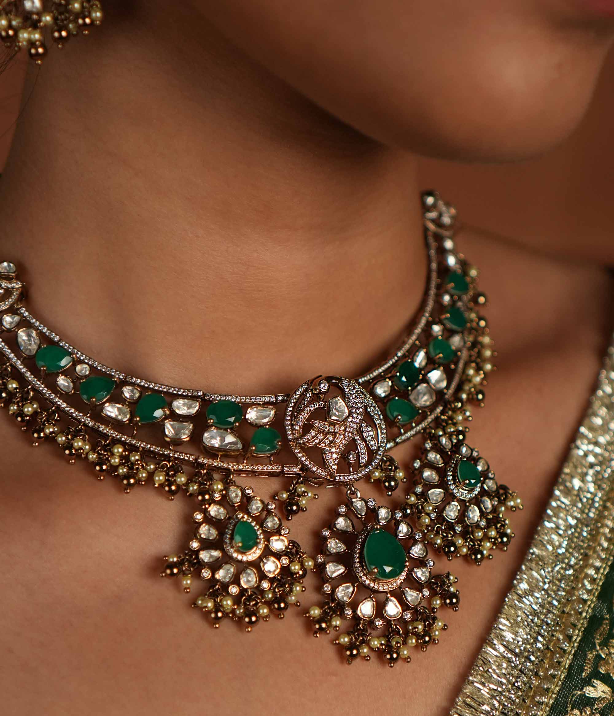 Victorian opulence reborn! This gold-plated silver choker necklace features a dazzling combination of CZ stones, green gemstones, and polki stones. The chain is adorned with polki and green gemstones, while the pendant mirrors the same design, gracefully accented with delicate pearl drops. A timeless blend of heritage and luxury, redefined for modern elegance.