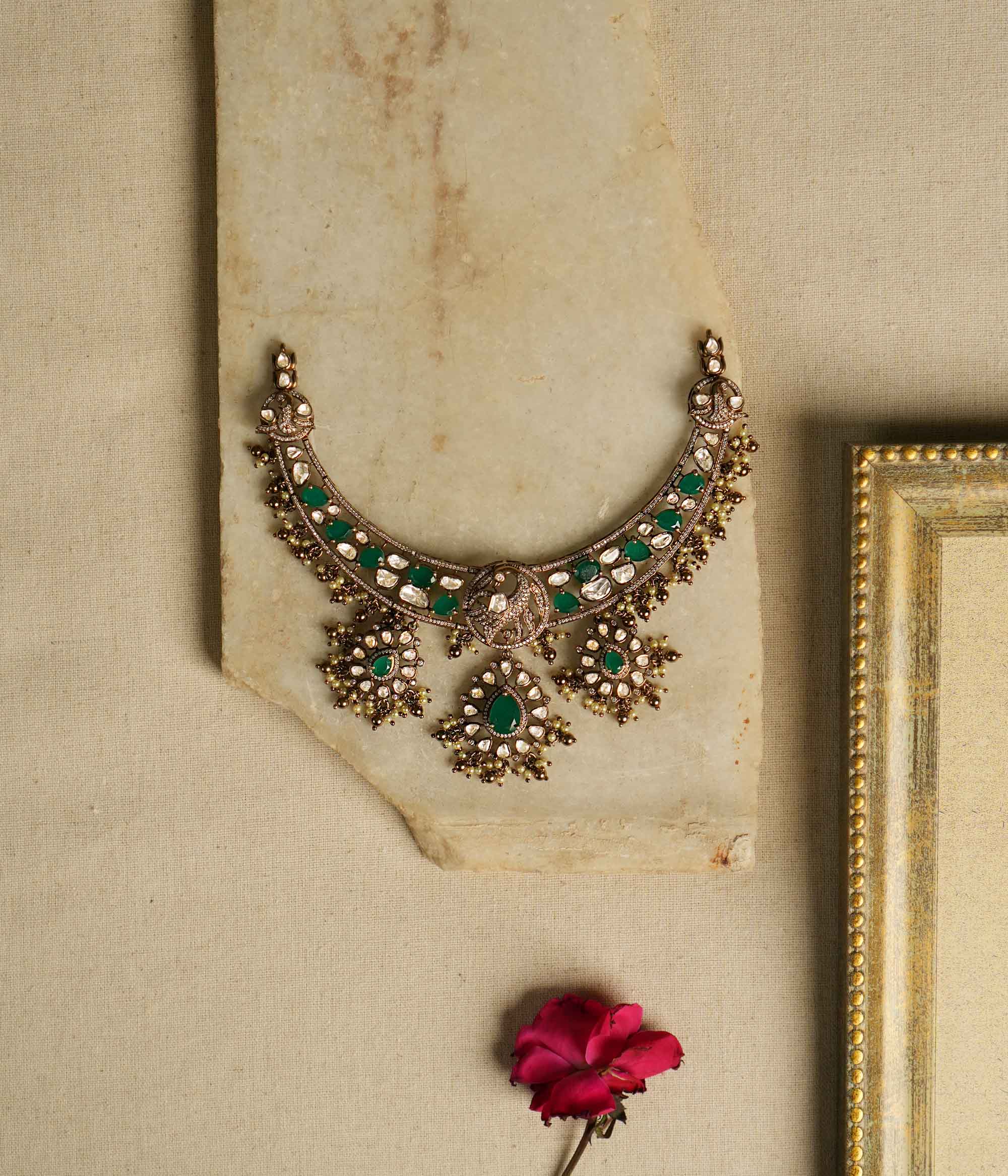 Victorian opulence reborn! This gold-plated silver choker necklace features a dazzling combination of CZ stones, green gemstones, and polki stones. The chain is adorned with polki and green gemstones, while the pendant mirrors the same design, gracefully accented with delicate pearl drops. A timeless blend of heritage and luxury, redefined for modern elegance.
