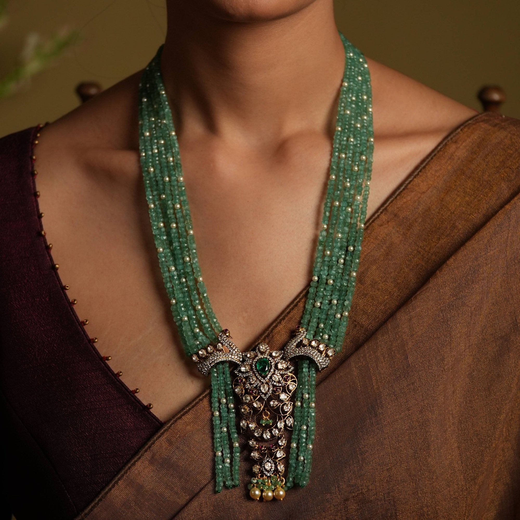 Green beaded necklace with a pendant on a person wearing a brown top.