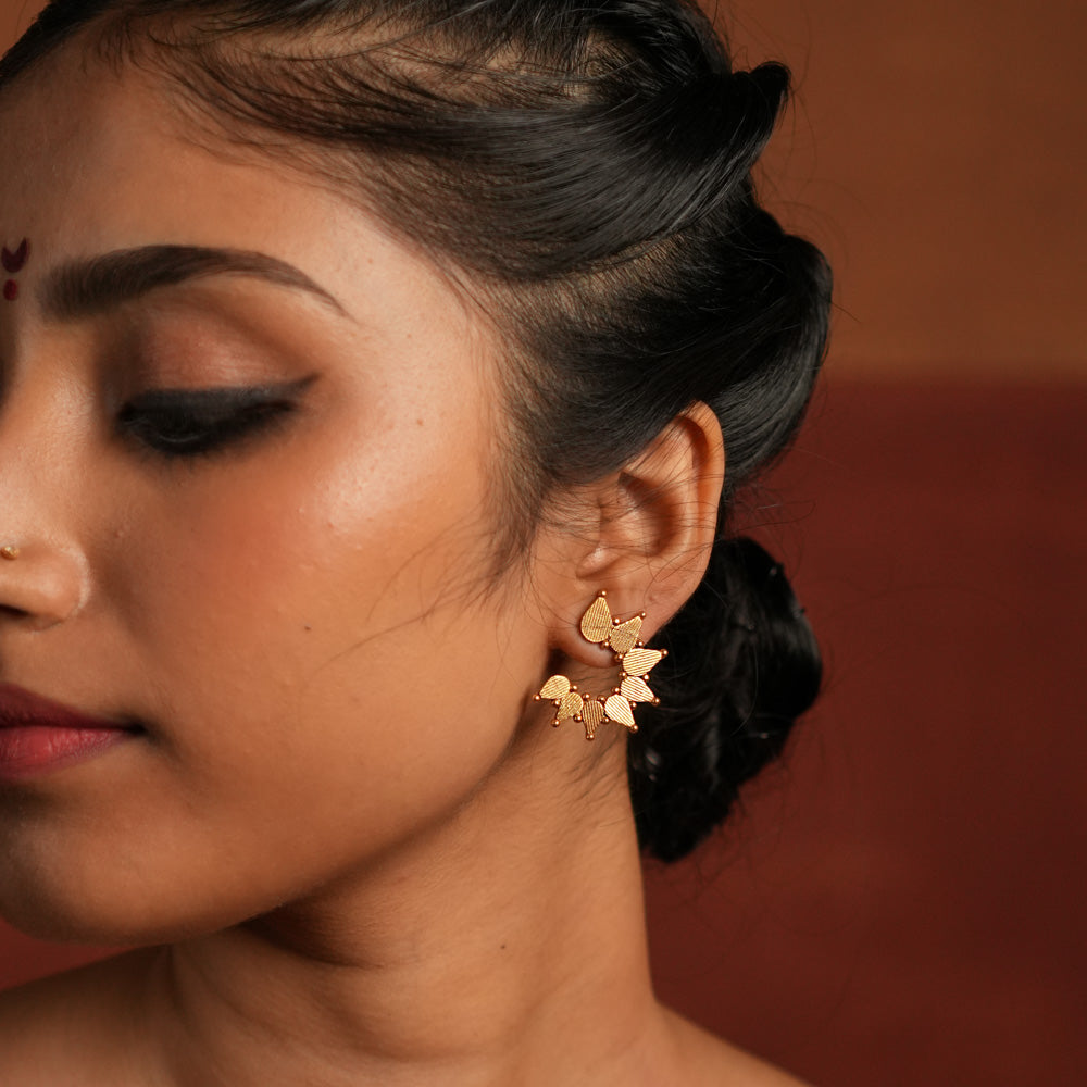 Gold-plated silver stud earrings featuring swirling leaf motifs intricately arranged in a circular dance, inspired by vintage Kolhapuri tribal designs. The detailed craftsmanship adds a touch of heritage charm, making them a timeless and elegant accessory.