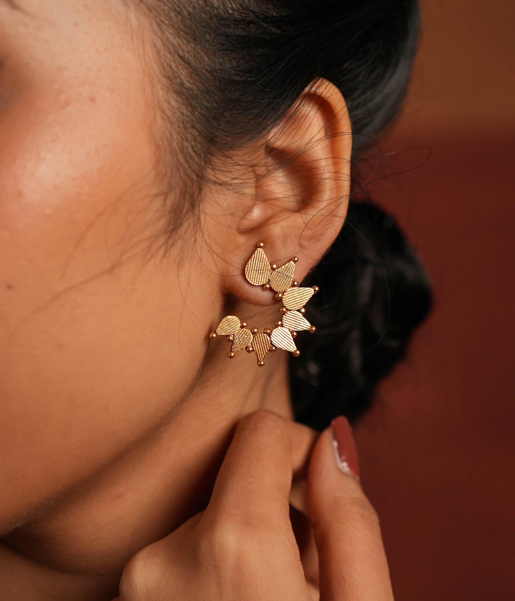 Gold-plated silver stud earrings featuring swirling leaf motifs intricately arranged in a circular dance, inspired by vintage Kolhapuri tribal designs. The detailed craftsmanship adds a touch of heritage charm, making them a timeless and elegant accessory.
