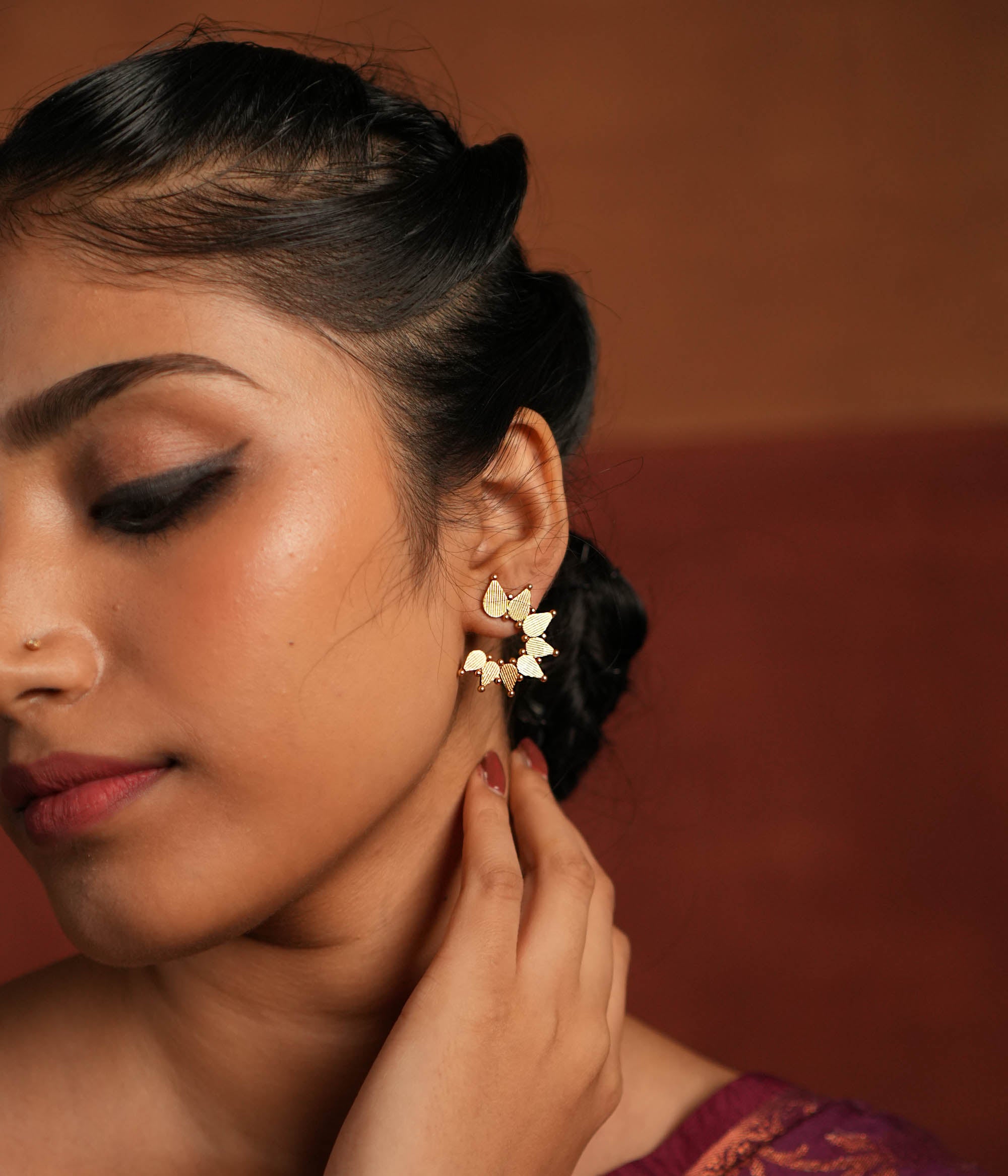 Gold-plated silver stud earrings featuring swirling leaf motifs intricately arranged in a circular dance, inspired by vintage Kolhapuri tribal designs. The detailed craftsmanship adds a touch of heritage charm, making them a timeless and elegant accessory.