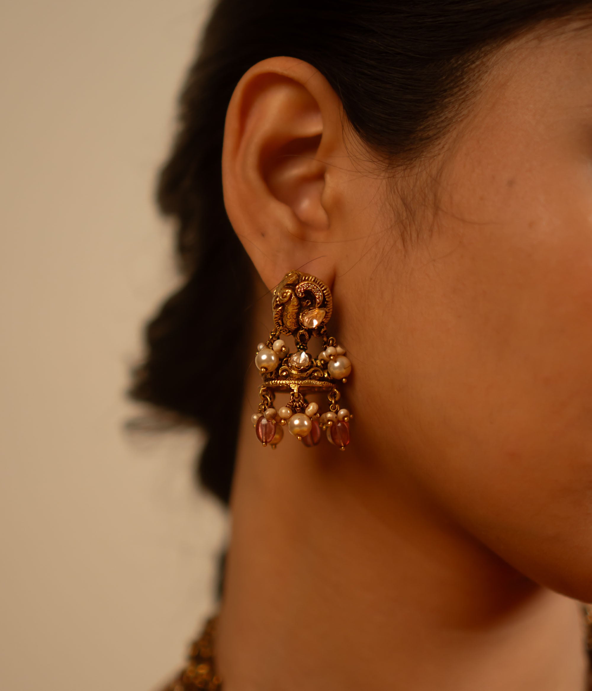 Handcrafted in antique gold-plated silver, these dangler earrings showcase a seamless fusion of classic elegance and modern charm. Adorned with white kundan stones, pearls, and red beads, their vintage-inspired design adds a timeless allure.