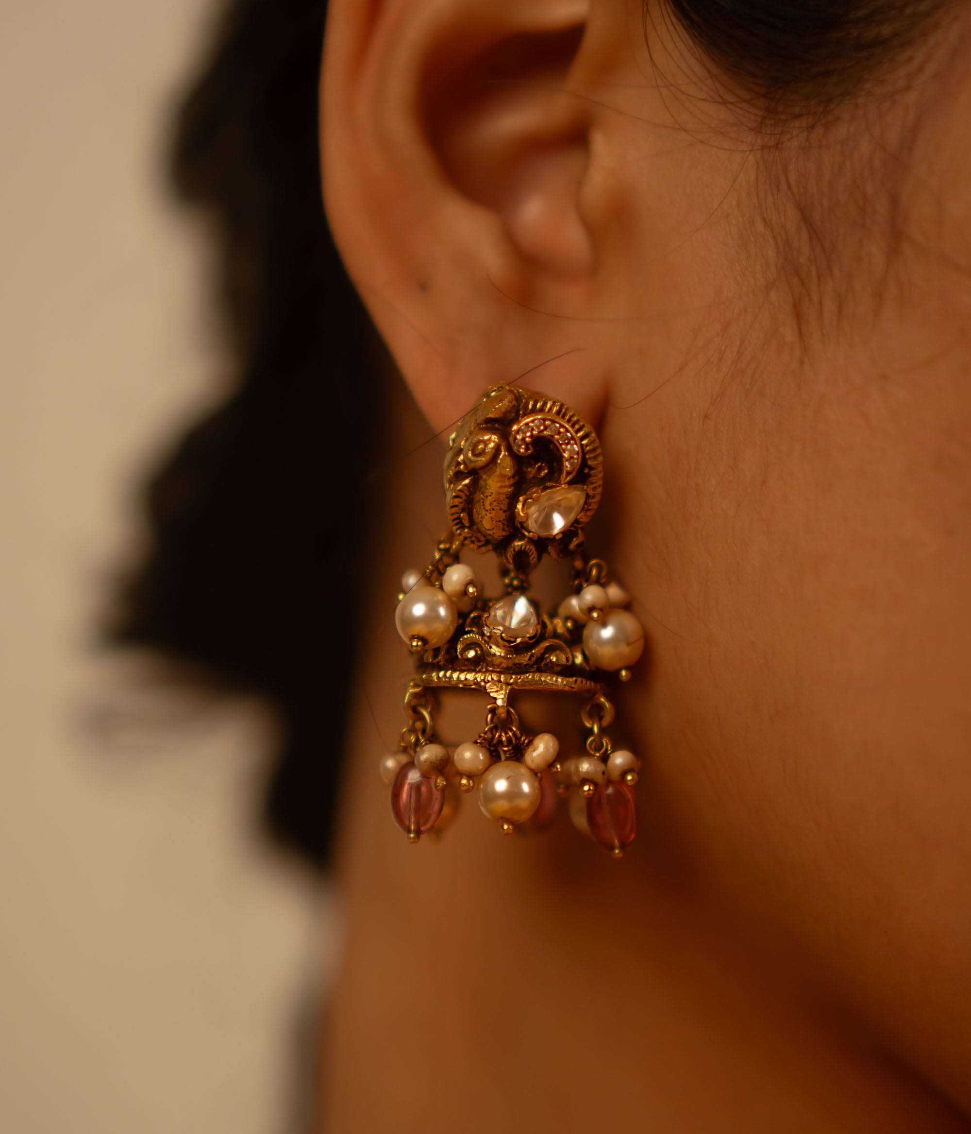 Handcrafted in antique gold-plated silver, these dangler earrings showcase a seamless fusion of classic elegance and modern charm. Adorned with white kundan stones, pearls, and red beads, their vintage-inspired design adds a timeless allure.