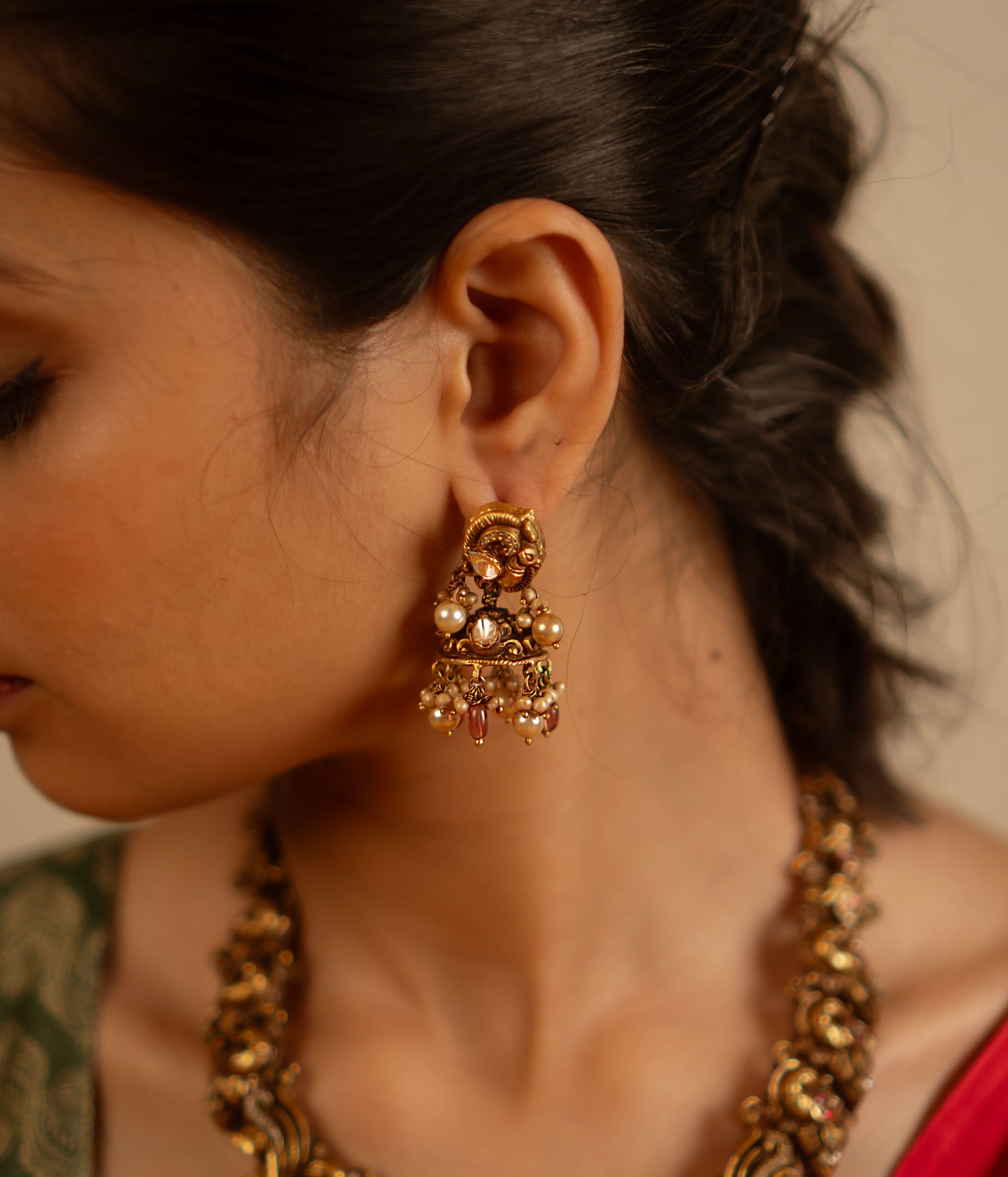 Handcrafted in antique gold-plated silver, these dangler earrings showcase a seamless fusion of classic elegance and modern charm. Adorned with white kundan stones, pearls, and red beads, their vintage-inspired design adds a timeless allure.