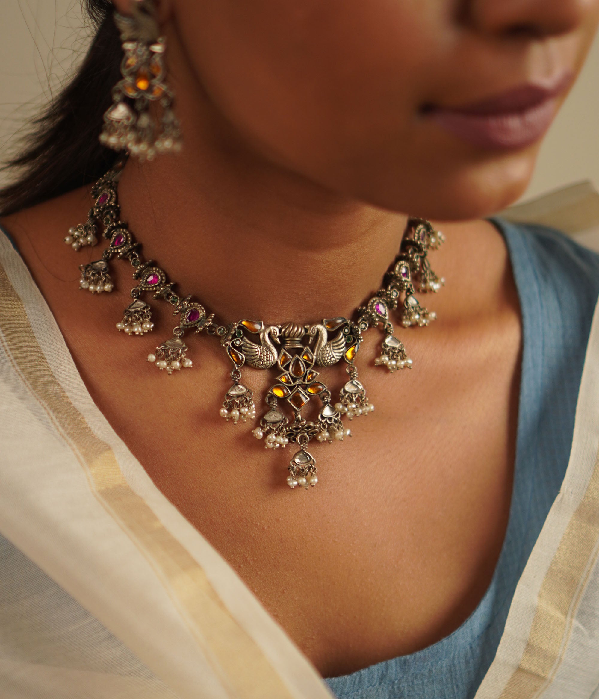 A cherished heirloom reimagined—the peacock-motif necklace in oxidized silver is adorned with radiant red and yellow kundan stones, finished with delicate pearl droplets. A timeless piece reminiscent of the treasured jewels passed down through generations.