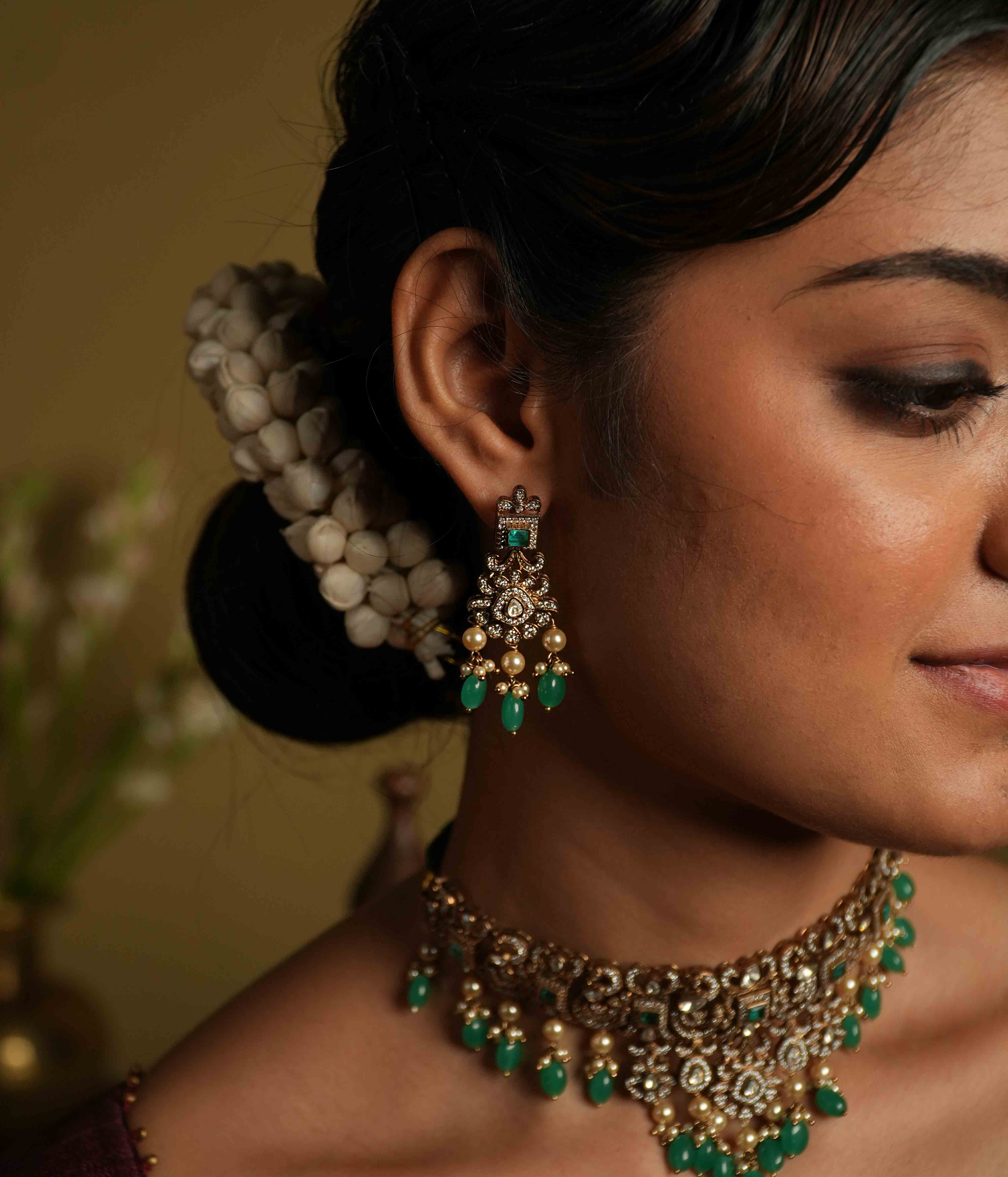 These intricate drop earrings, crafted from 92.5 sterling silver and featuring Bombay screw fastenings, showcase moissanite and bold green gemstones, complemented by delicate pearl dangles that evoke the opulence of a Victorian era.