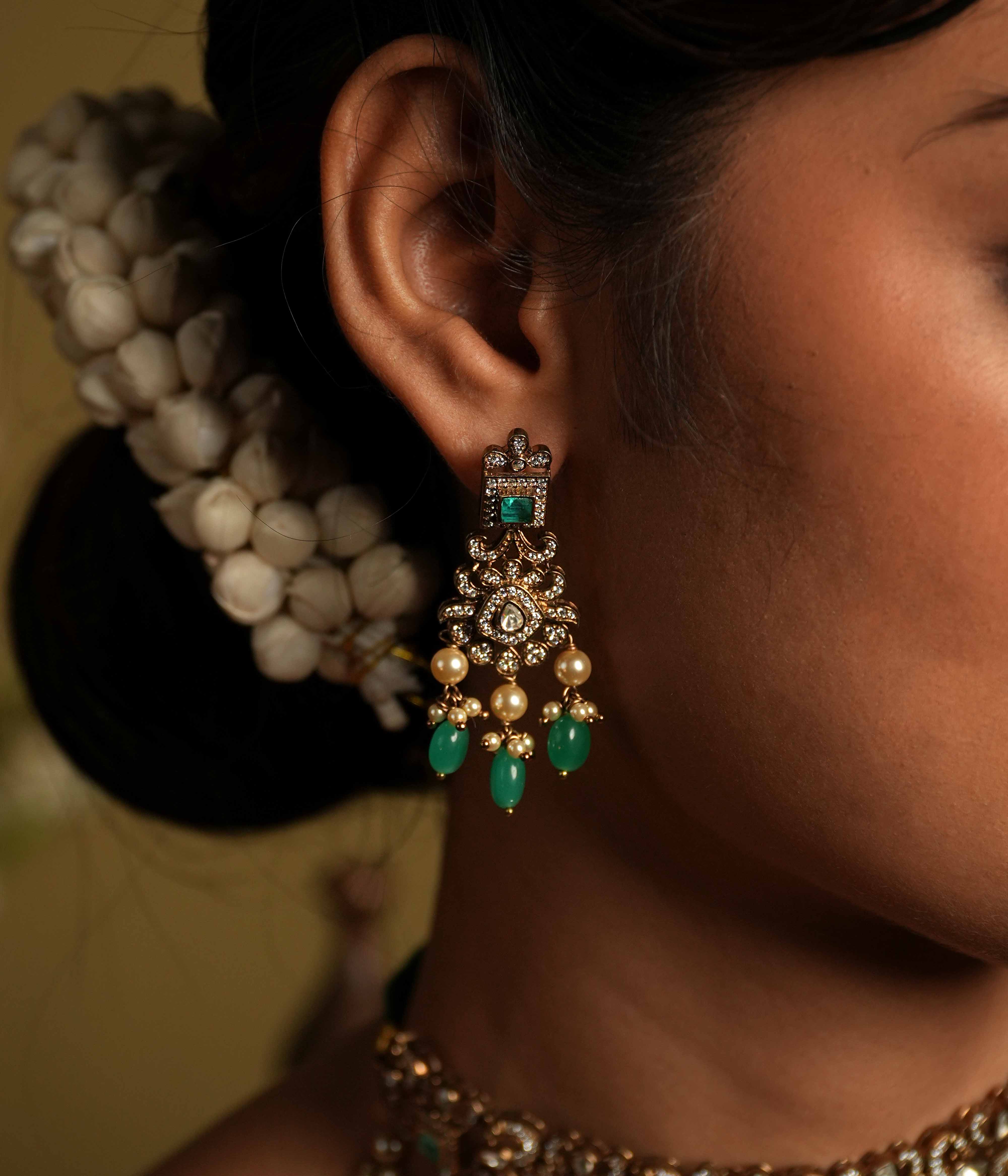 These intricate drop earrings, crafted from 92.5 sterling silver and featuring Bombay screw fastenings, showcase moissanite and bold green gemstones, complemented by delicate pearl dangles that evoke the opulence of a Victorian era.