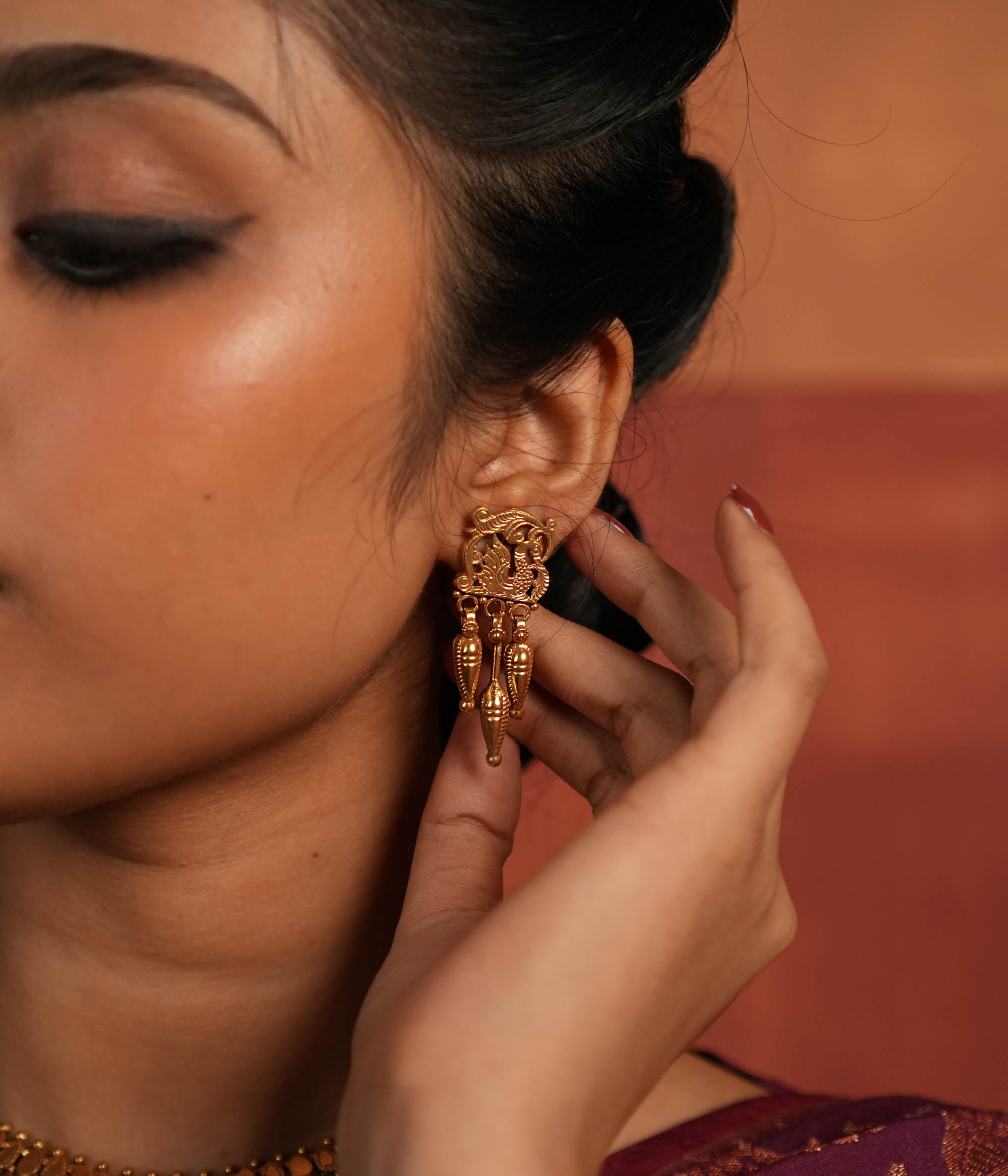 Tribal Majesty Reborn. These gold-plated silver dangler earrings, featuring a delicate peacock motif in the stud and a spike-like pendant with intricate designs, draw inspiration from vintage Kolhapuri artistry, blending timeless tradition with contemporary elegance.