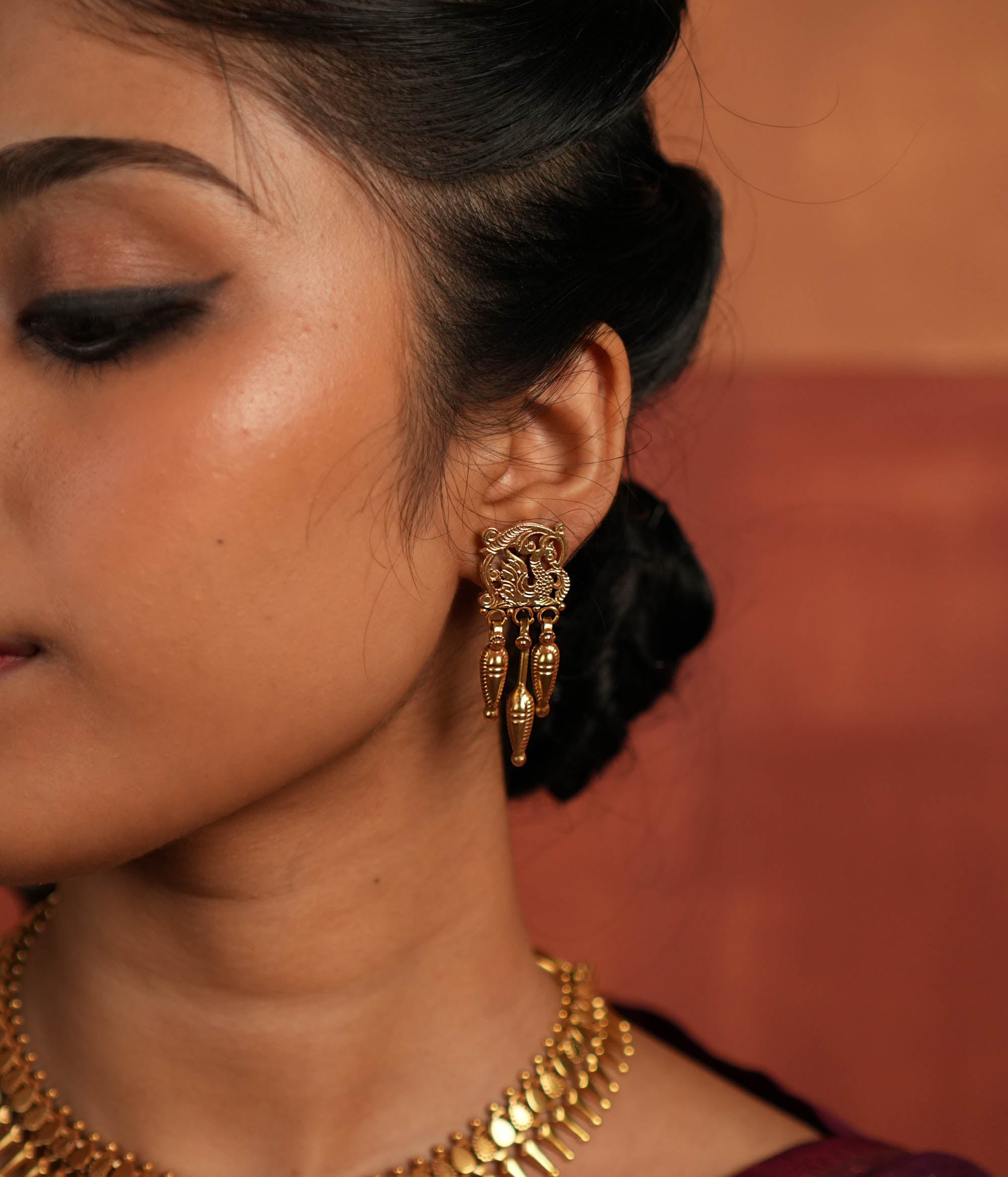 Tribal Majesty Reborn. These gold-plated silver dangler earrings, featuring a delicate peacock motif in the stud and a spike-like pendant with intricate designs, draw inspiration from vintage Kolhapuri artistry, blending timeless tradition with contemporary elegance.