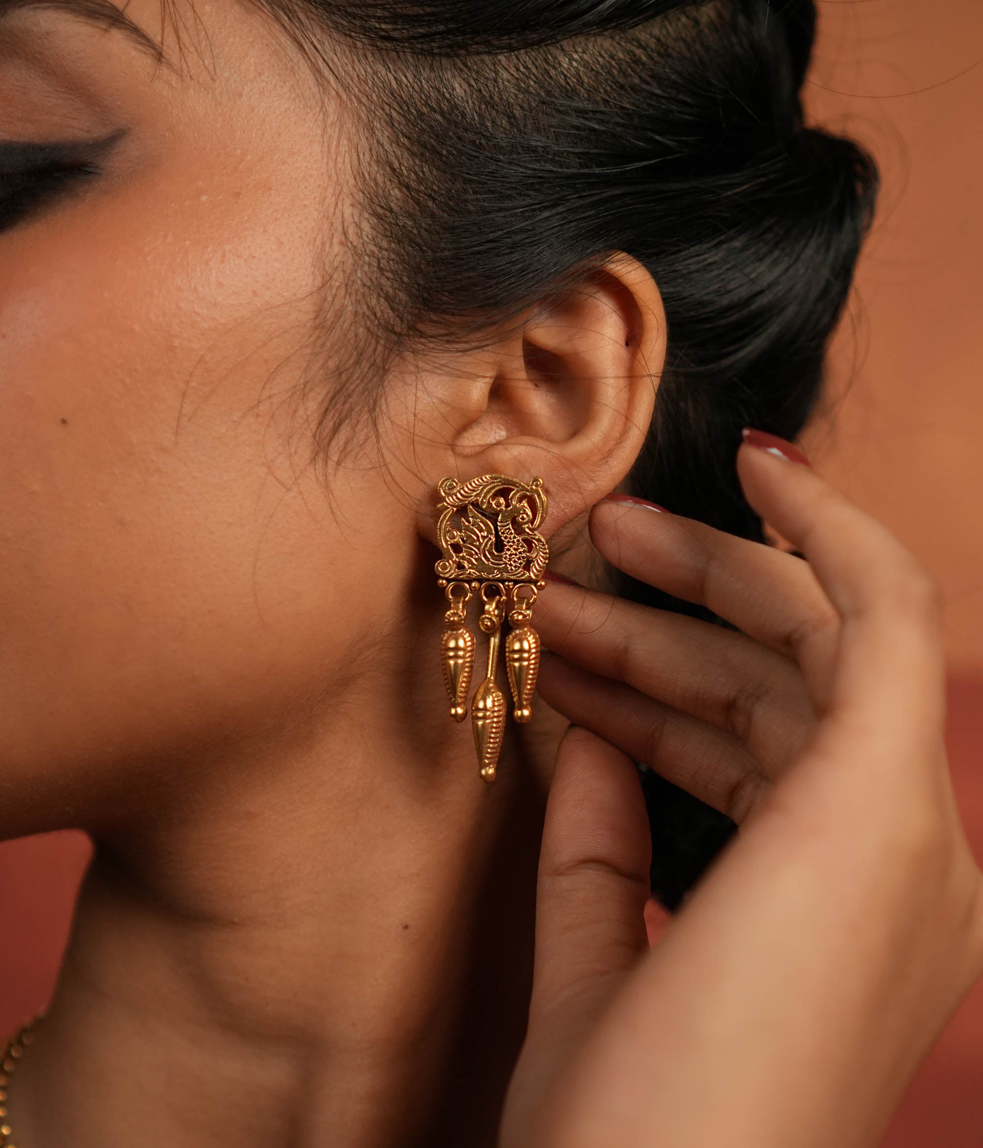 Tribal Majesty Reborn. These gold-plated silver dangler earrings, featuring a delicate peacock motif in the stud and a spike-like pendant with intricate designs, draw inspiration from vintage Kolhapuri artistry, blending timeless tradition with contemporary elegance.
