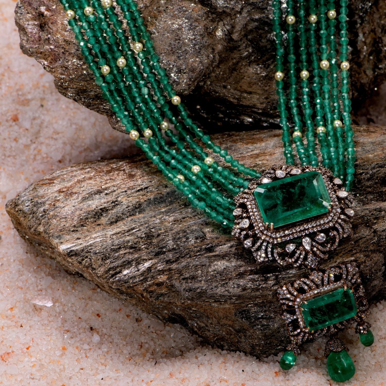 Elegant gold-plated silver necklace featuring a chain crafted from alternating green beads and white pearls. The centerpiece is a striking square-shaped green cut stone, encased in a delicate floral-shaped design adorned with CZ stones. Enhancing its beauty, the pendant also showcases a gracefully suspended green cut stone drop, surrounded by shimmering CZ stones, and green beads adding a sophisticated and timeless appeal.