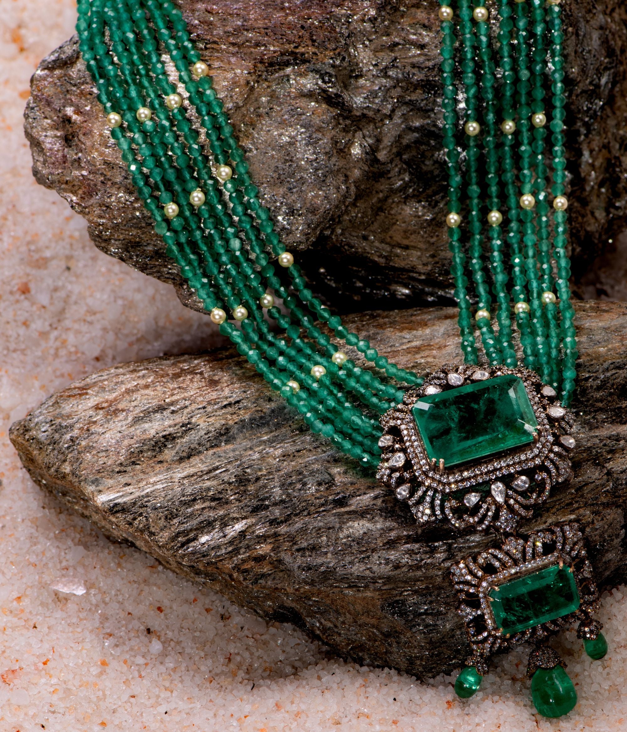 Elegant gold-plated silver necklace featuring a chain crafted from alternating green beads and white pearls. The centerpiece is a striking square-shaped green cut stone, encased in a delicate floral-shaped design adorned with CZ stones. Enhancing its beauty, the pendant also showcases a gracefully suspended green cut stone drop, surrounded by shimmering CZ stones, and green beads adding a sophisticated and timeless appeal.