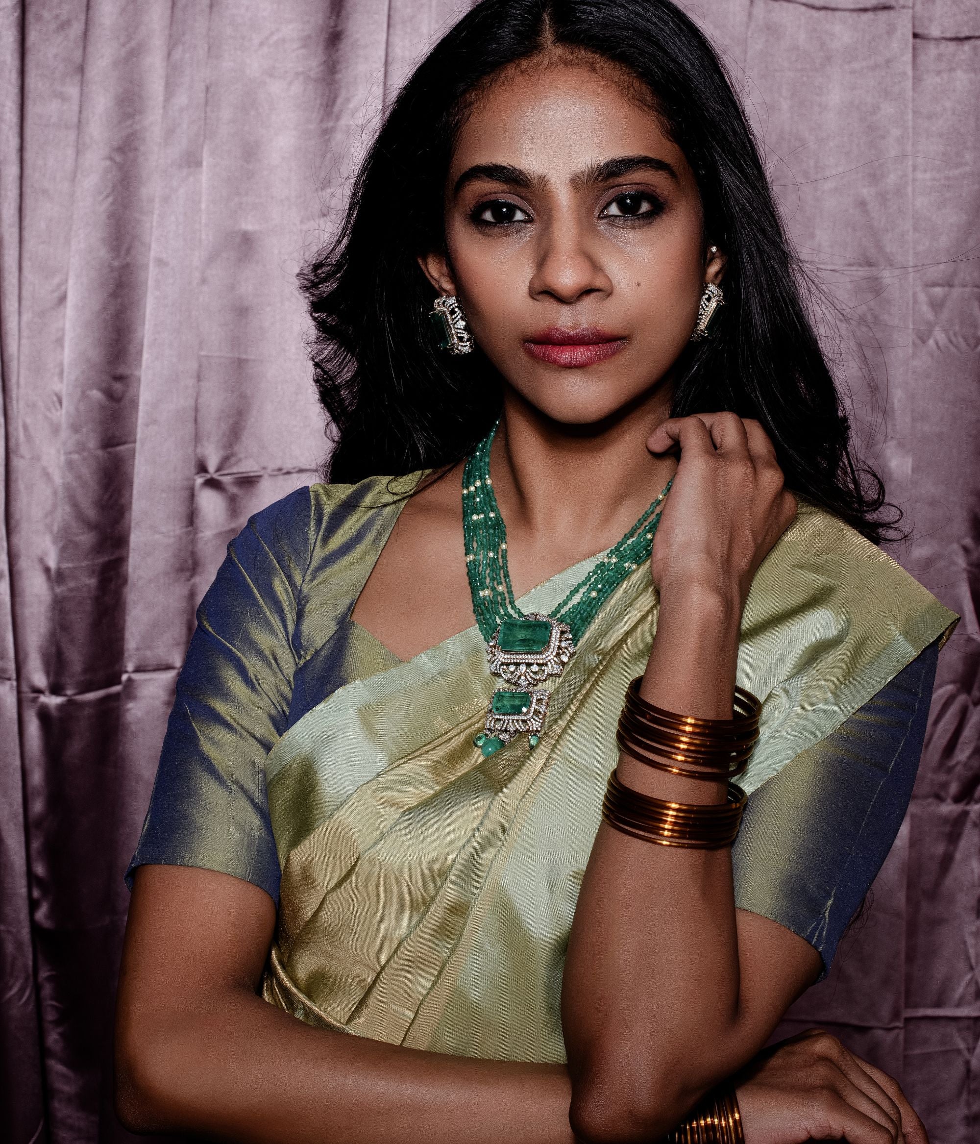 Elegant gold-plated silver necklace featuring a chain crafted from alternating green beads and white pearls. The centerpiece is a striking square-shaped green cut stone, encased in a delicate floral-shaped design adorned with CZ stones. Enhancing its beauty, the pendant also showcases a gracefully suspended green cut stone drop, surrounded by shimmering CZ stones, and green beads adding a sophisticated and timeless appeal.
