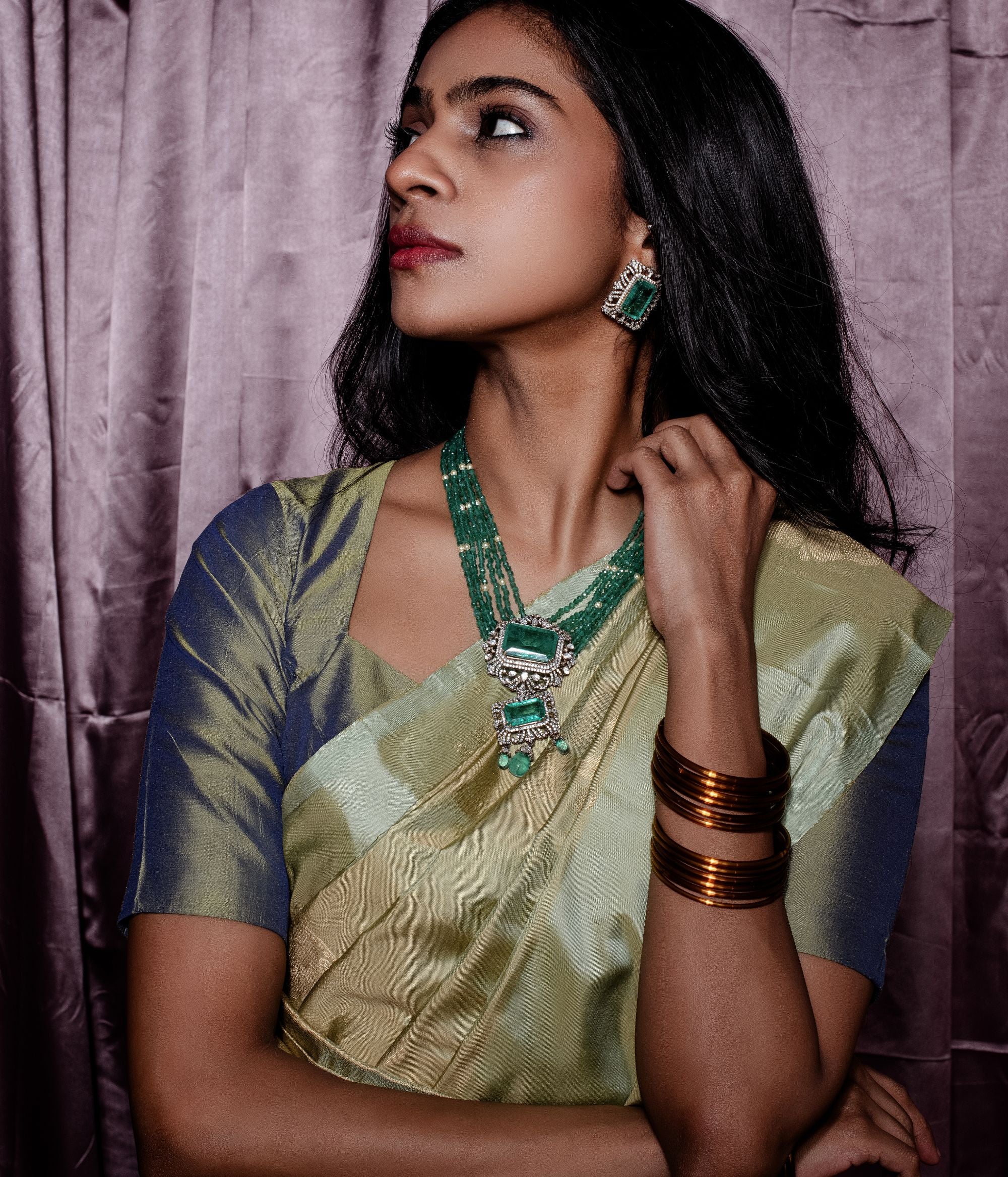 Elegant gold-plated silver necklace featuring a chain crafted from alternating green beads and white pearls. The centerpiece is a striking square-shaped green cut stone, encased in a delicate floral-shaped design adorned with CZ stones. Enhancing its beauty, the pendant also showcases a gracefully suspended green cut stone drop, surrounded by shimmering CZ stones, and green beads adding a sophisticated and timeless appeal.