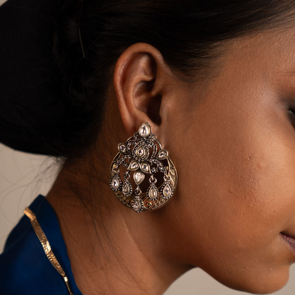 The Gurhal earrings showcase delicate floral patterns in oxidized silver, beautifully enhanced by the intricate brilliance of white Kundan stones.