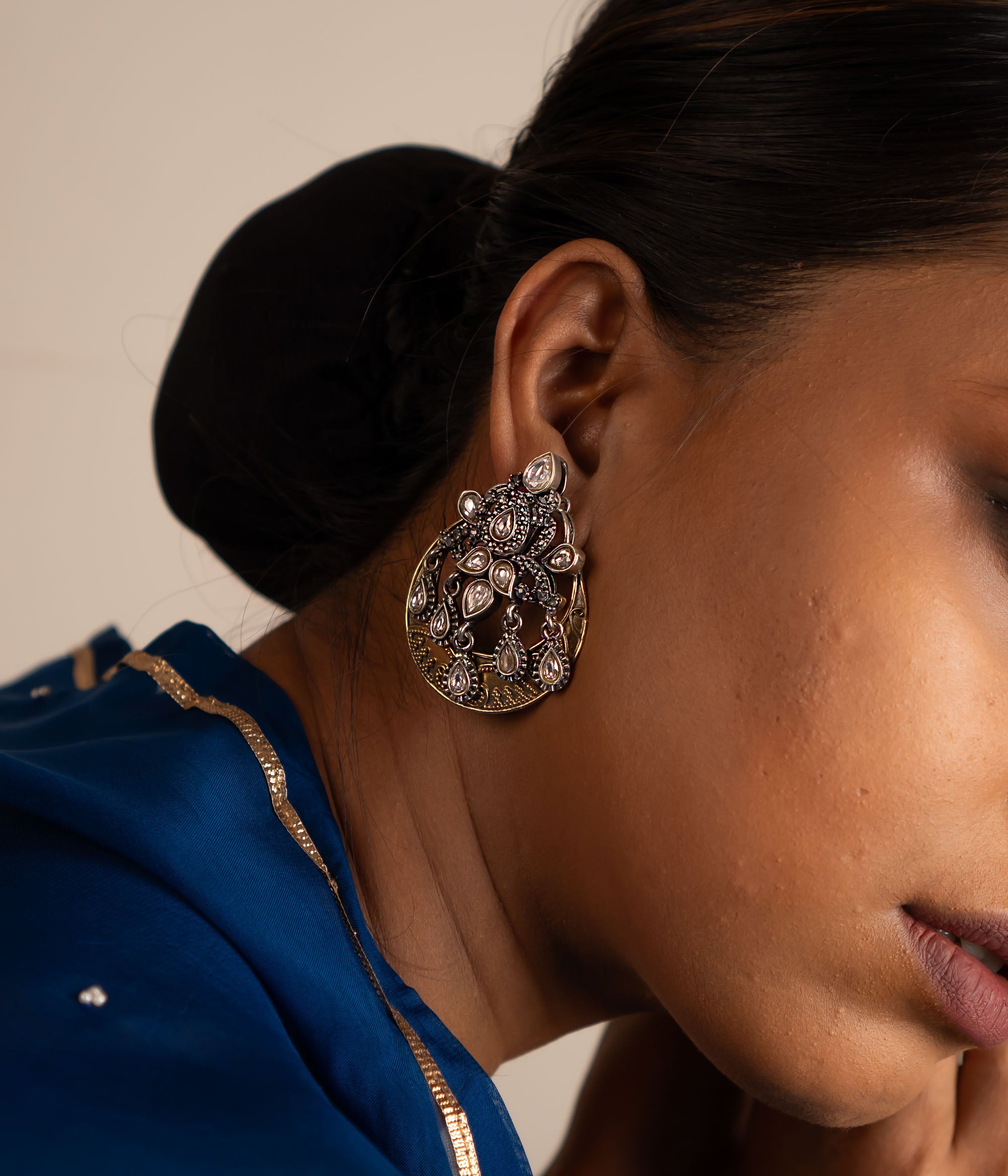 The Gurhal earrings showcase delicate floral patterns in oxidized silver, beautifully enhanced by the intricate brilliance of white Kundan stones.
