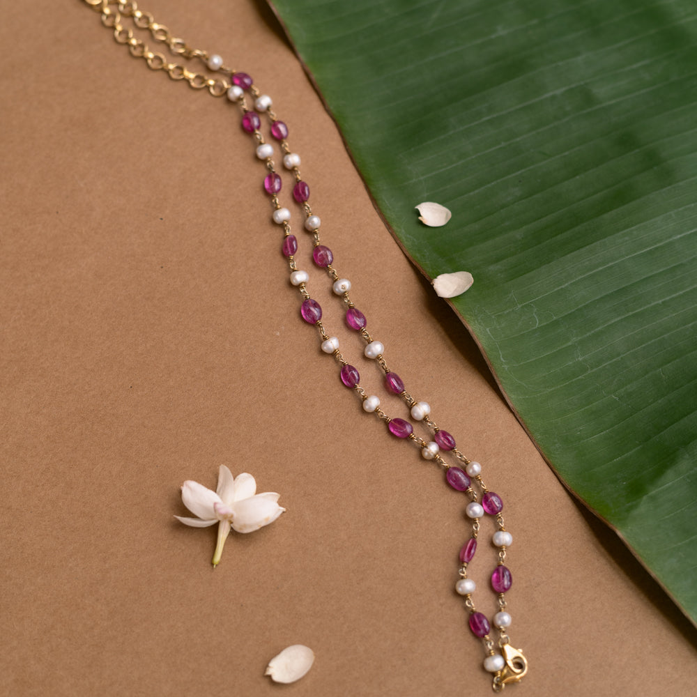 A two-strand necklace with one strand of red beads and the other of pearls.