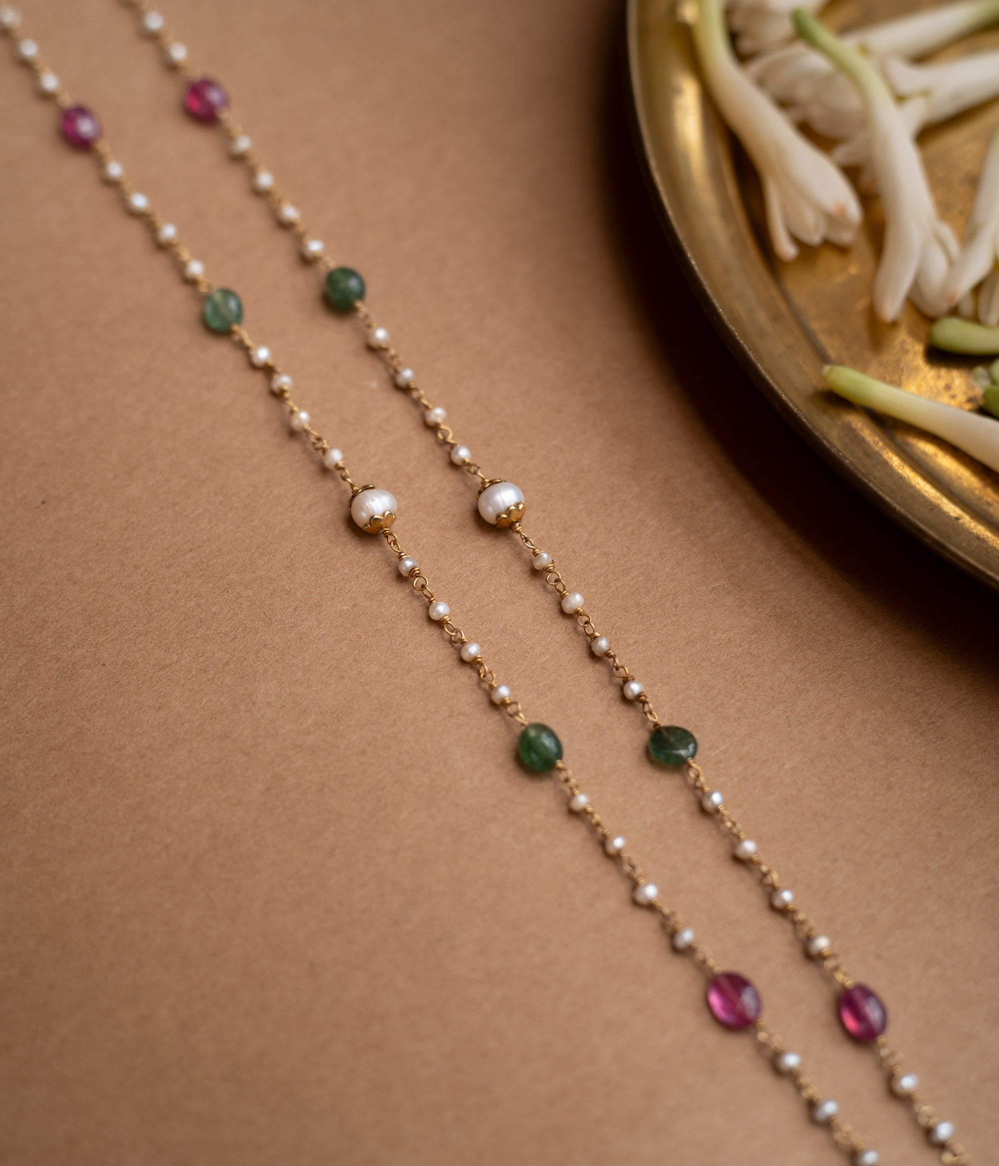 A three-tiered chain with one strand of red beads, one of green beads, and a final strand of pearls.