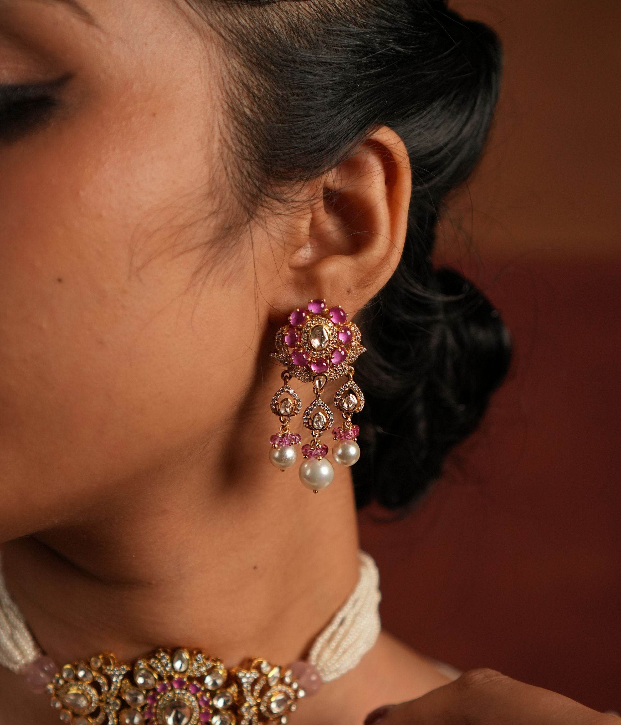 A stunning gold-plated silver dangler earring featuring Moissanite Polki stones and Rose Quartz. The stud showcases a delicate floral design crafted with Rose Quartz, while the elegant drop is adorned with a shimmering Polki stone covered by cz stones , gracefully complemented by white pearls and soft pink beads. This exquisite piece adds a touch of elegance and charm, perfect for a timeless look.