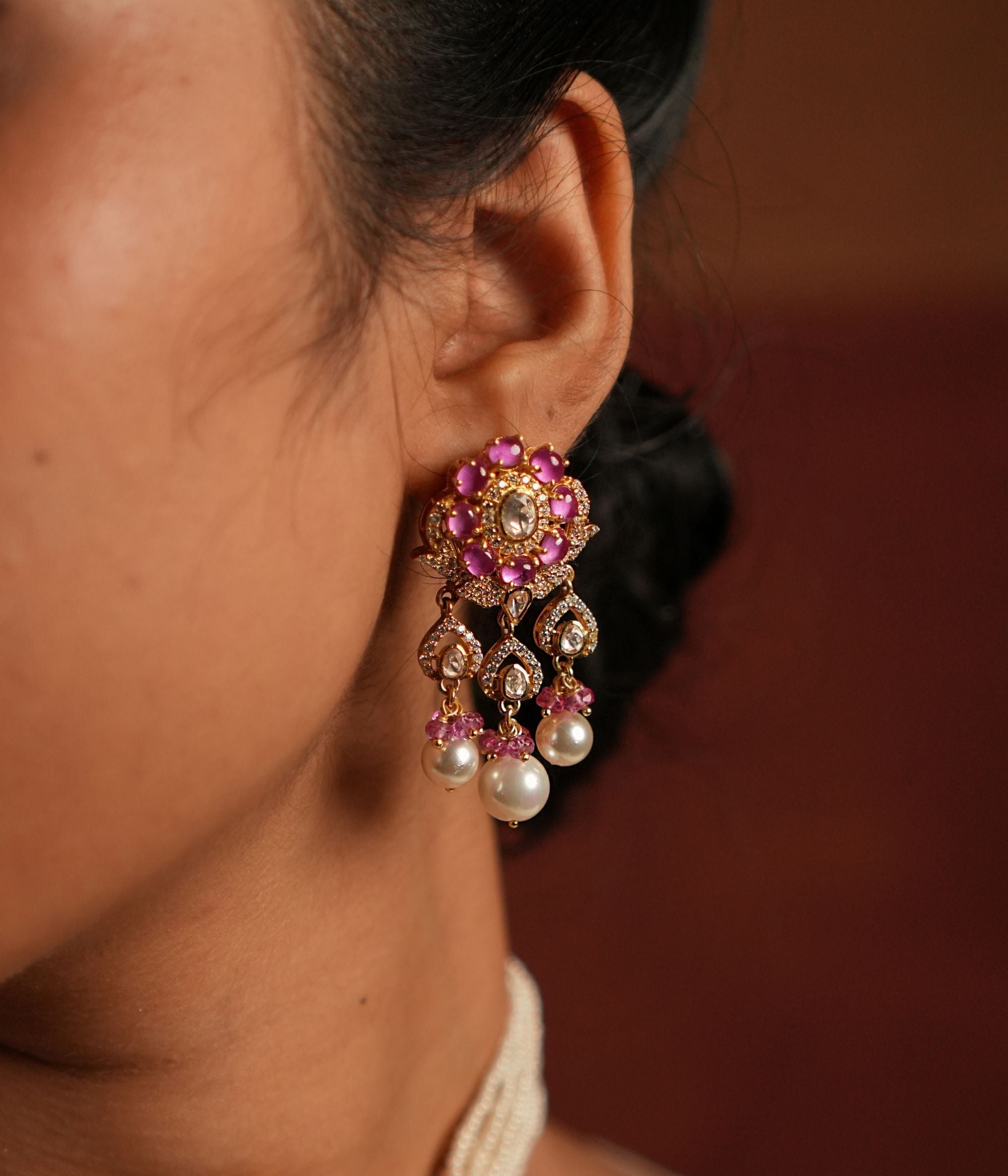 A stunning gold-plated silver dangler earring featuring Moissanite Polki stones and Rose Quartz. The stud showcases a delicate floral design crafted with Rose Quartz, while the elegant drop is adorned with a shimmering Polki stone covered by cz stones , gracefully complemented by white pearls and soft pink beads. This exquisite piece adds a touch of elegance and charm, perfect for a timeless look.