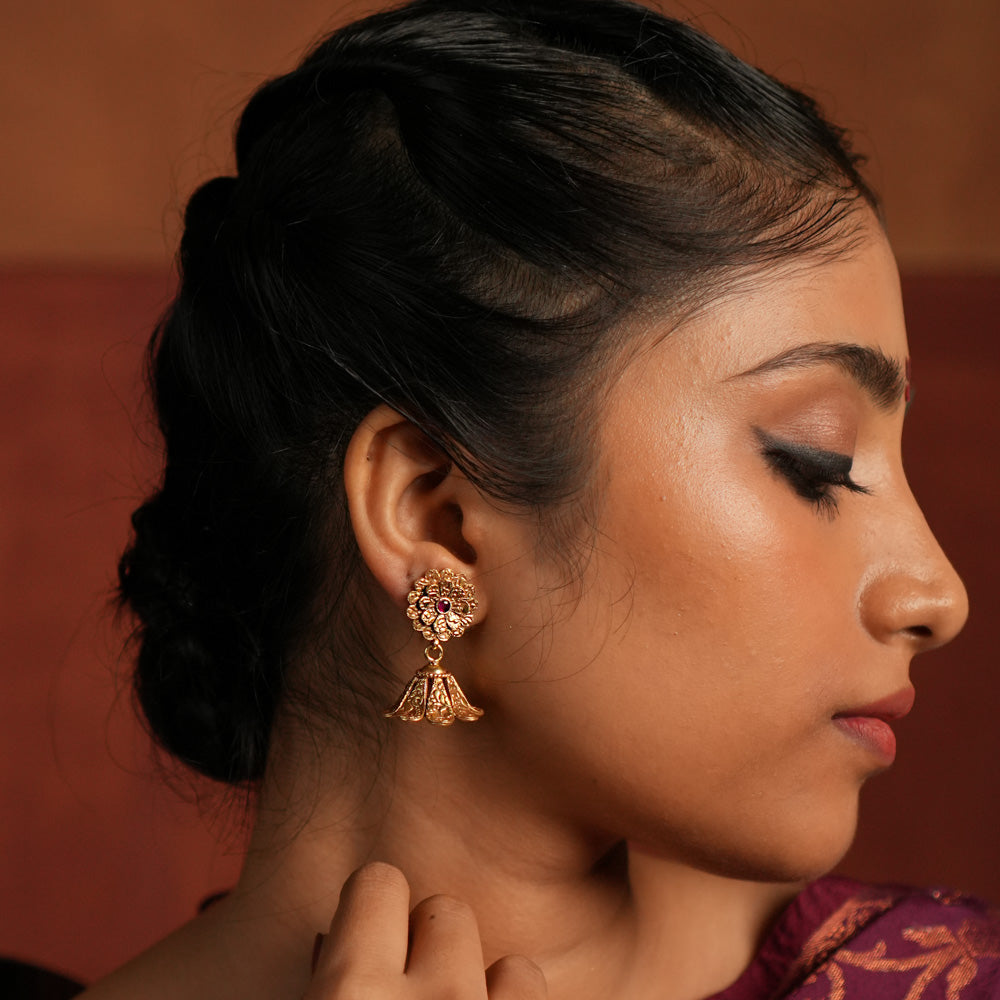 Exquisite jhumka earrings featuring a floral design engraved with intricate tiny floral details. The centerpiece showcases a striking red Kundan stone, enhancing the elegance of the design. The jhumka structure adds a traditional touch, making it a timeless statement piece.
