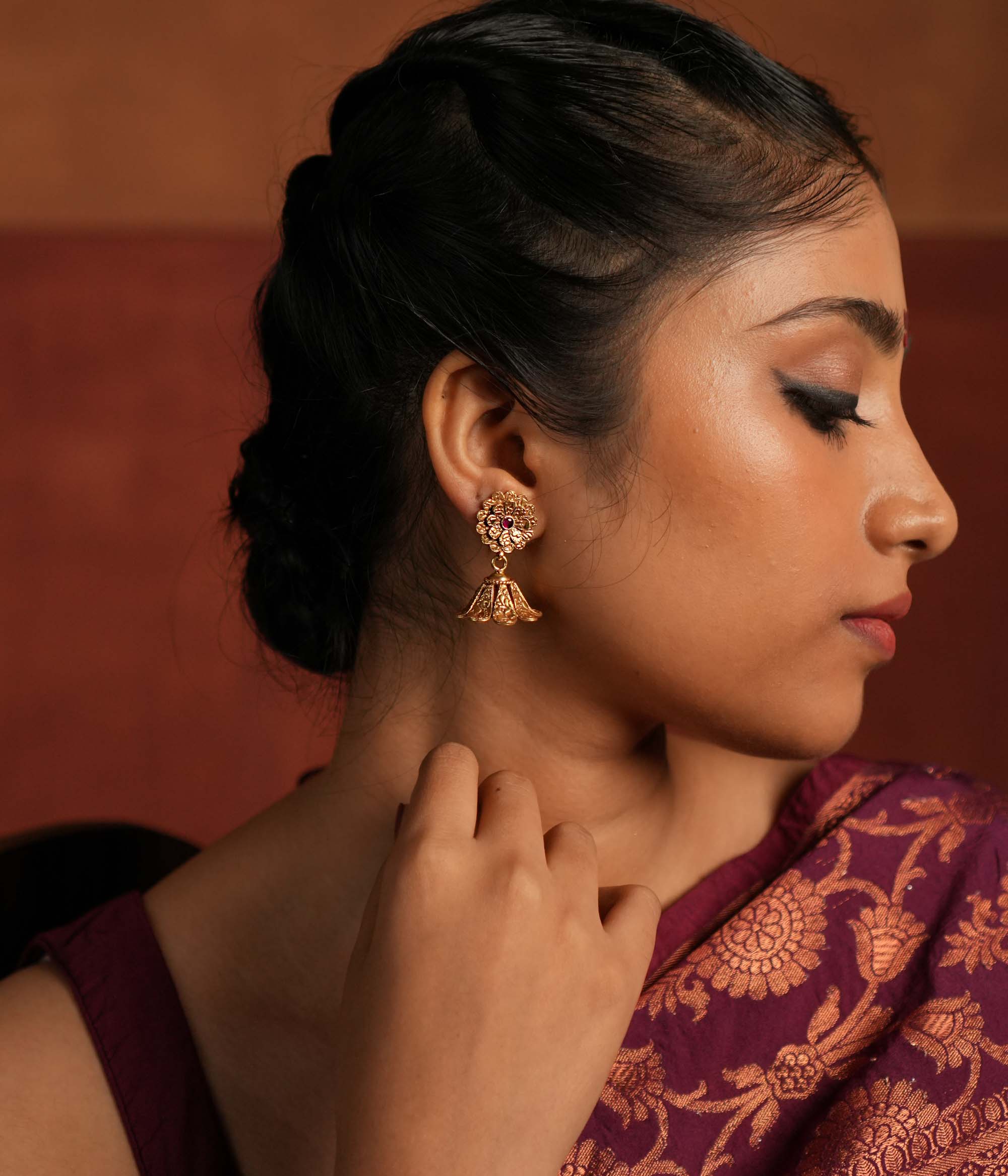 Exquisite jhumka earrings featuring a floral design engraved with intricate tiny floral details. The centerpiece showcases a striking red Kundan stone, enhancing the elegance of the design. The jhumka structure adds a traditional touch, making it a timeless statement piece.