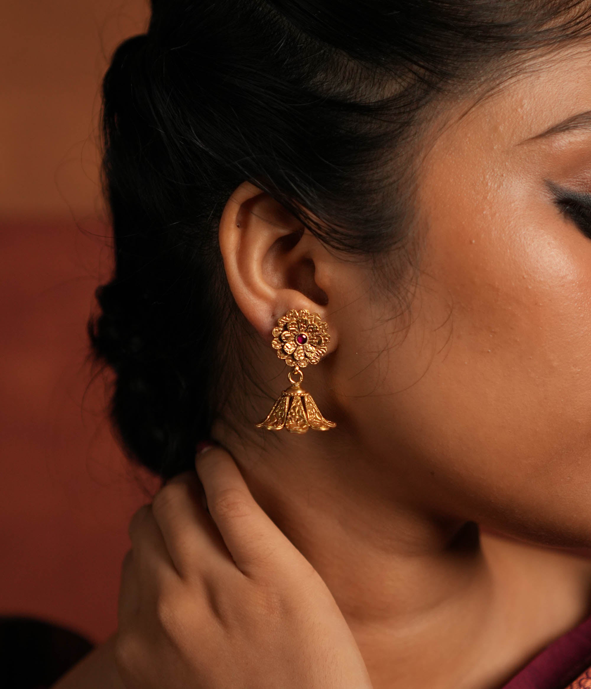 Exquisite jhumka earrings featuring a floral design engraved with intricate tiny floral details. The centerpiece showcases a striking red Kundan stone, enhancing the elegance of the design. The jhumka structure adds a traditional touch, making it a timeless statement piece.