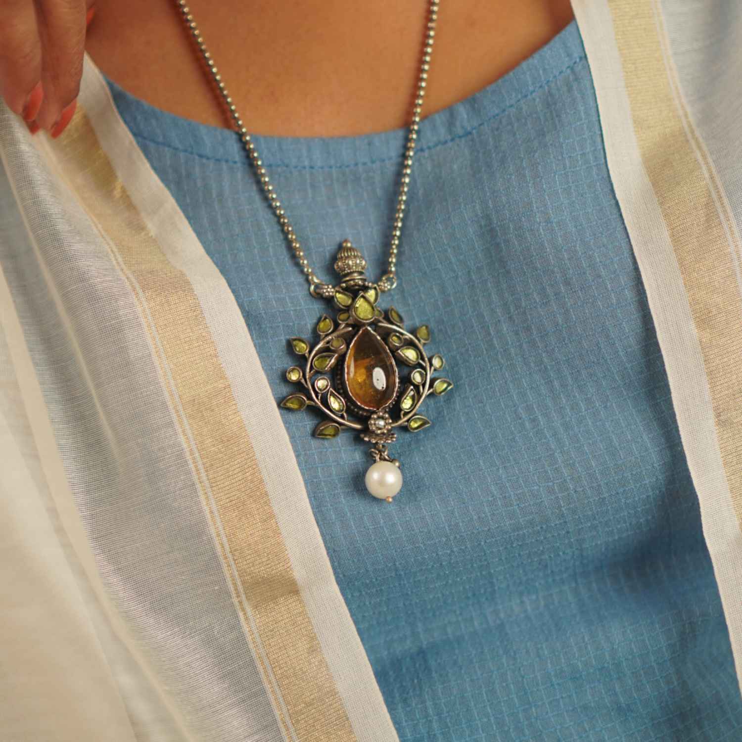 This vintage-inspired silver pendant, suspended from a delicate beaded chain, features radiant yellow kundan, warm amber stones, and luminous pearls. Handcrafted with precision and care, it celebrates the charm of artisanal craftsmanship and the beauty of unique imperfections.