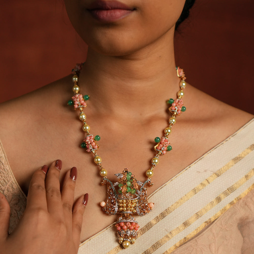 A gold-plated silver necklace adorned with Moissanite Polki stones, Swarovski crystals, green gemstones, coral beads, freshwater pearls, and green strawberry quartz beads. The intricate pendant showcases exquisite craftsmanship, blending traditional and contemporary design elements for a statement look.