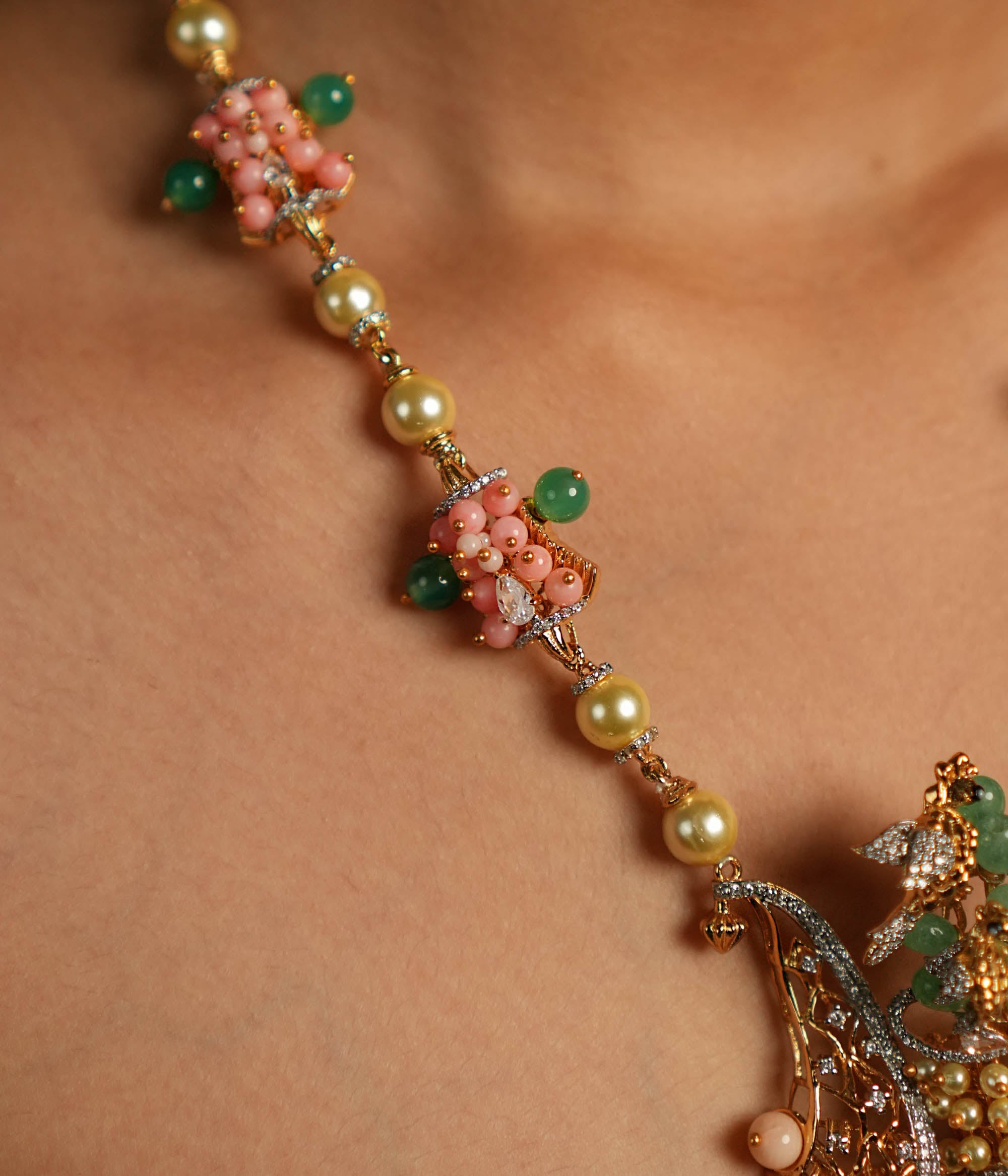 A gold-plated silver necklace adorned with Moissanite Polki stones, Swarovski crystals, green gemstones, coral beads, freshwater pearls, and green strawberry quartz beads. The intricate pendant showcases exquisite craftsmanship, blending traditional and contemporary design elements for a statement look.